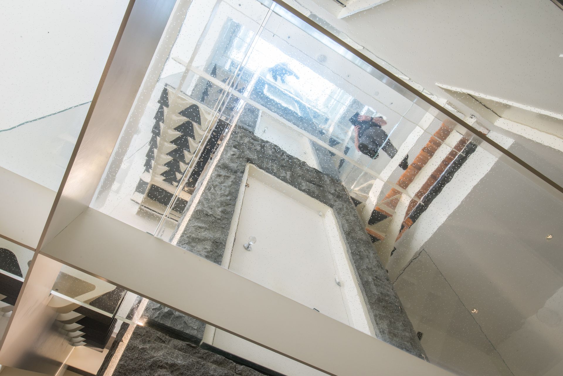 Glass-walled interior atrium with a central staircase and reflections of windows and railings