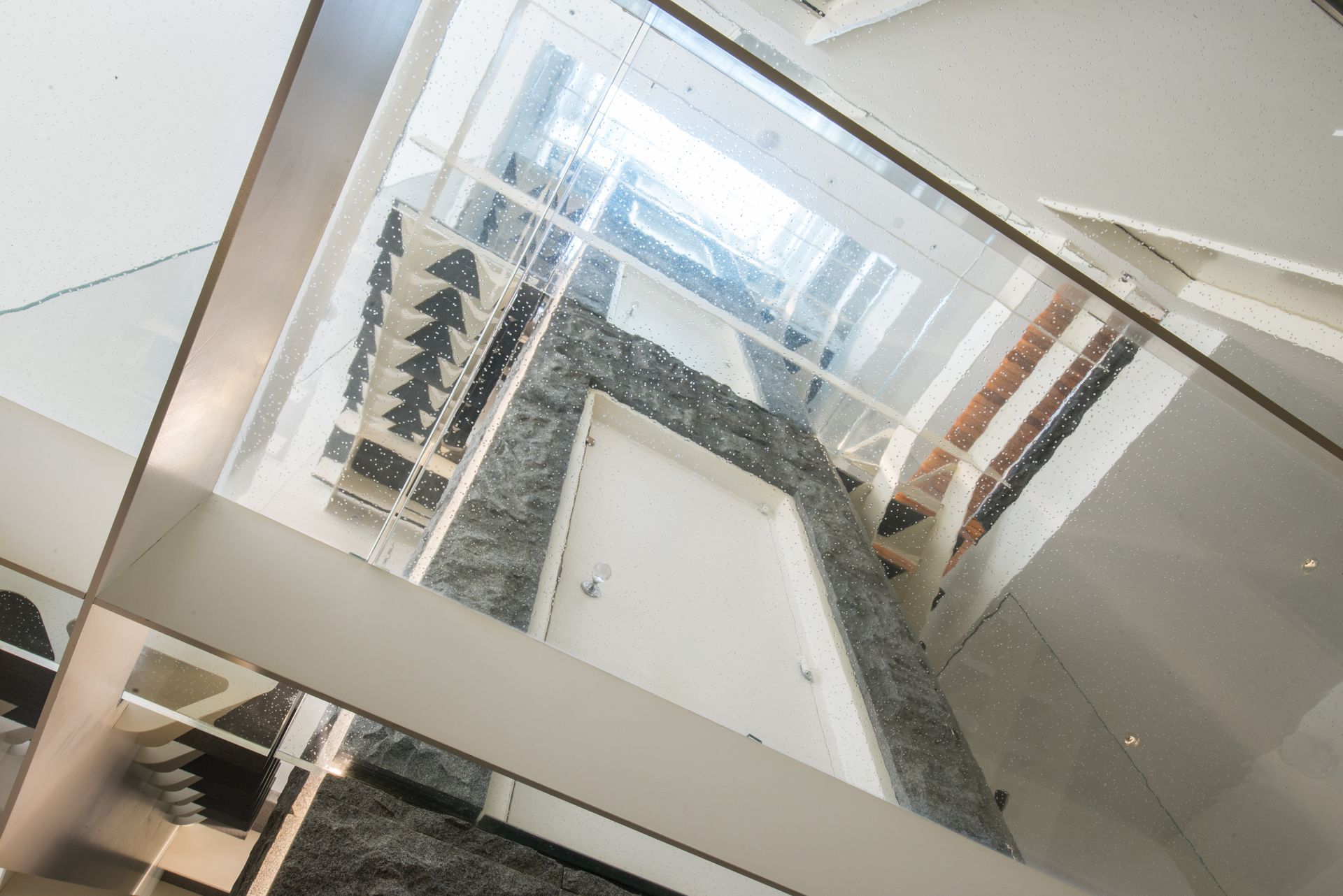 Looking up a stairwell with white walls, black railings, and skylight reflections.