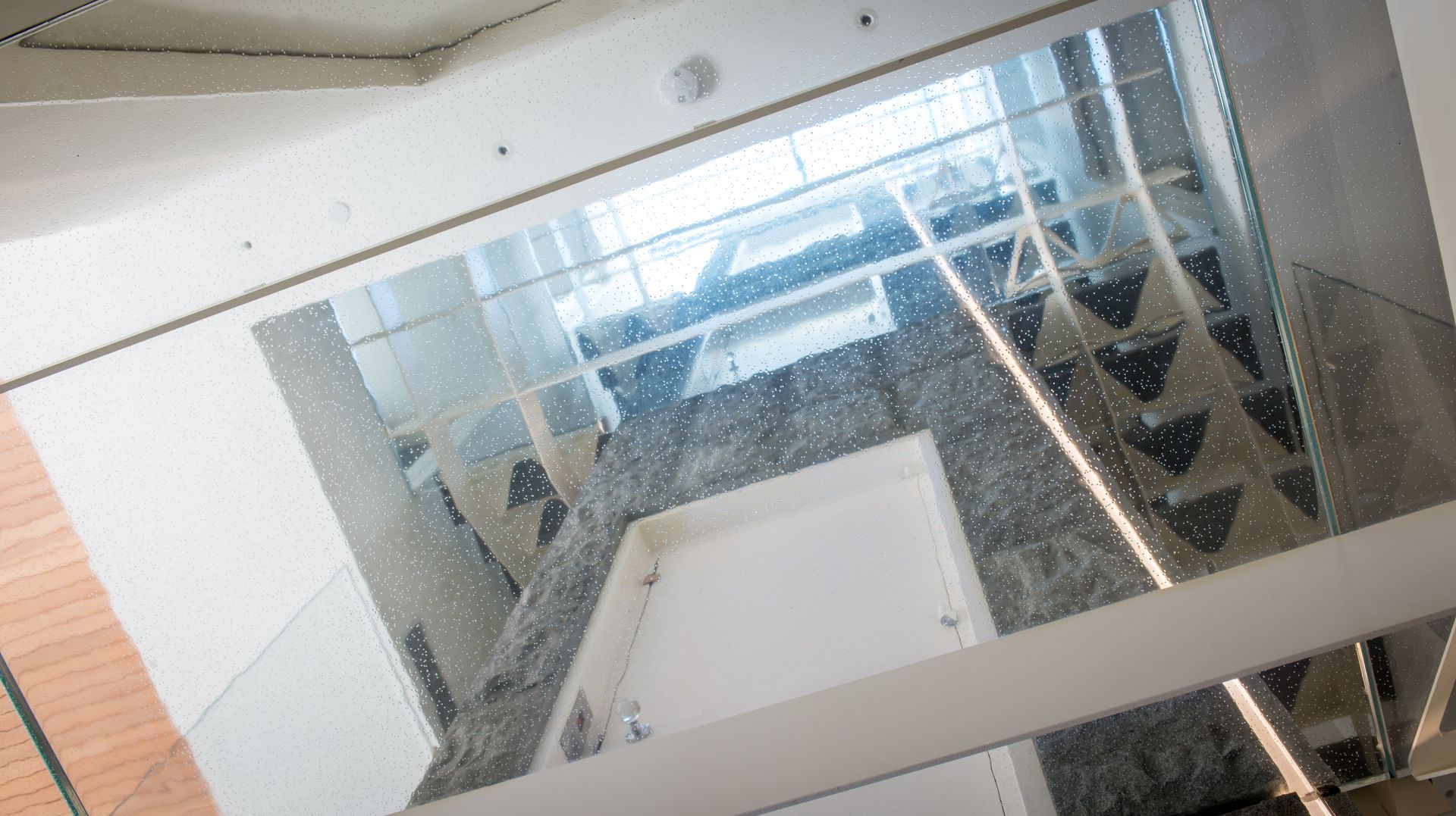 Glass stairwell with white walls and reflective panels, viewed from above