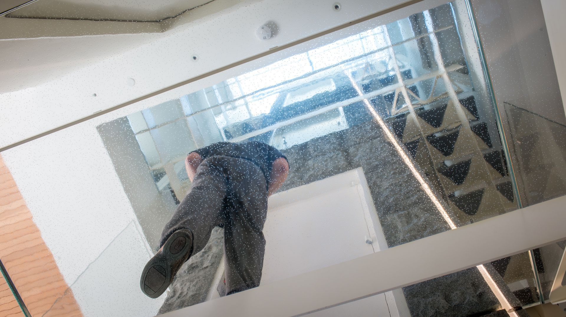 Person standing on a glass staircase, viewed from above in a modern interior.