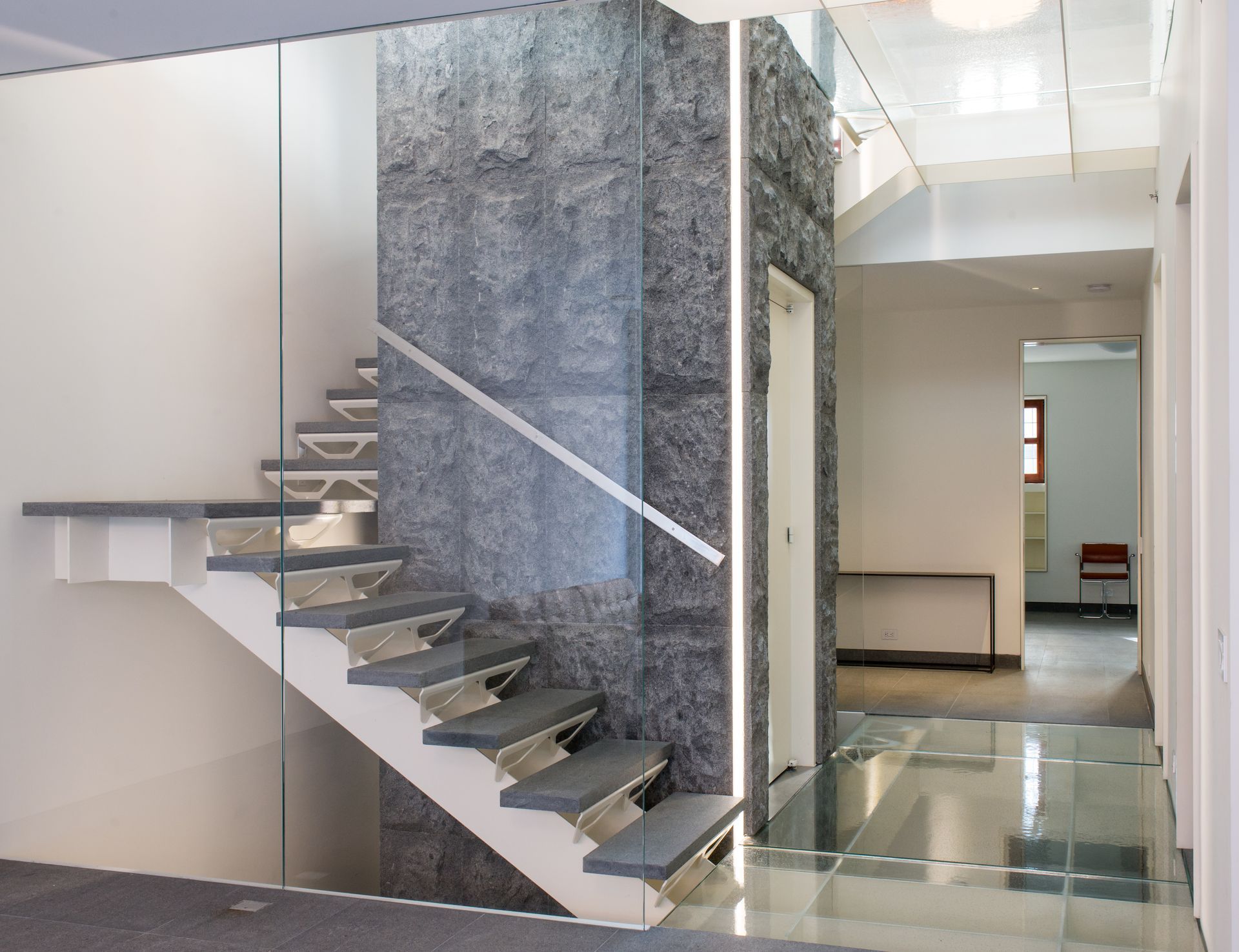 Modern interior staircase with glass railing and polished stone finishes in a bright hallway