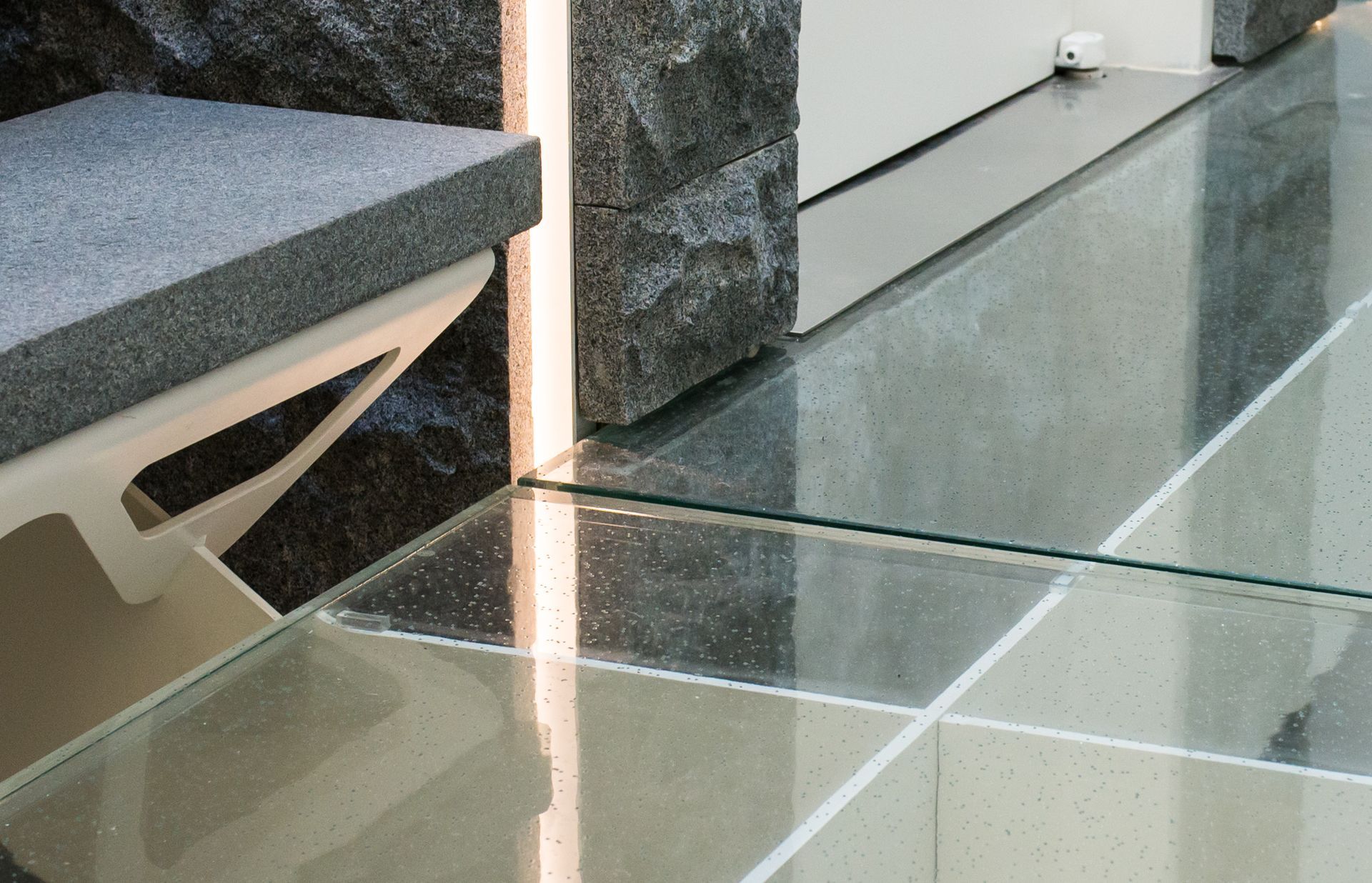 Modern glass floor beside a bench and stone wall indoors
