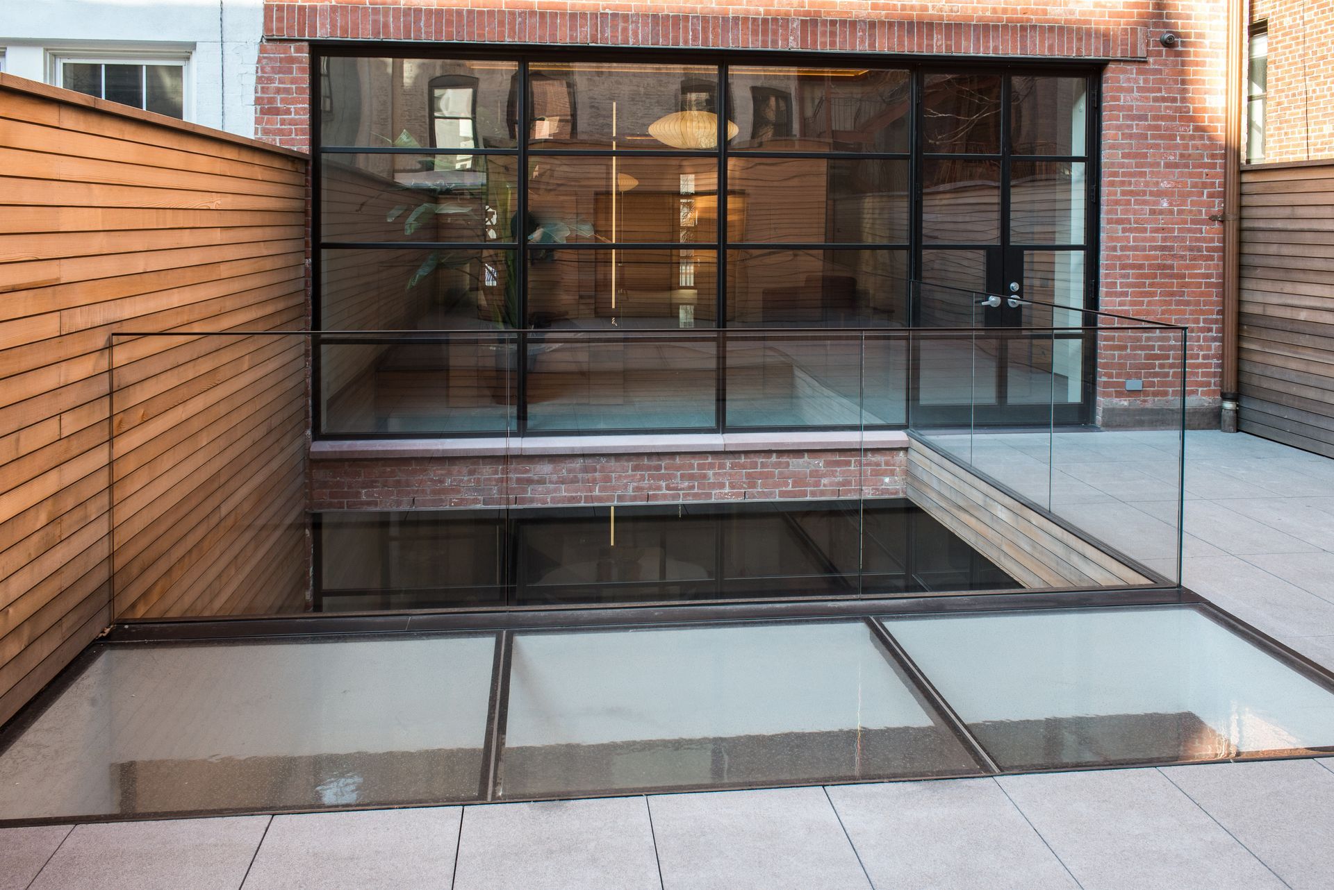 Modern brick courtyard with large black-framed windows and a sunken glass-covered lightwell