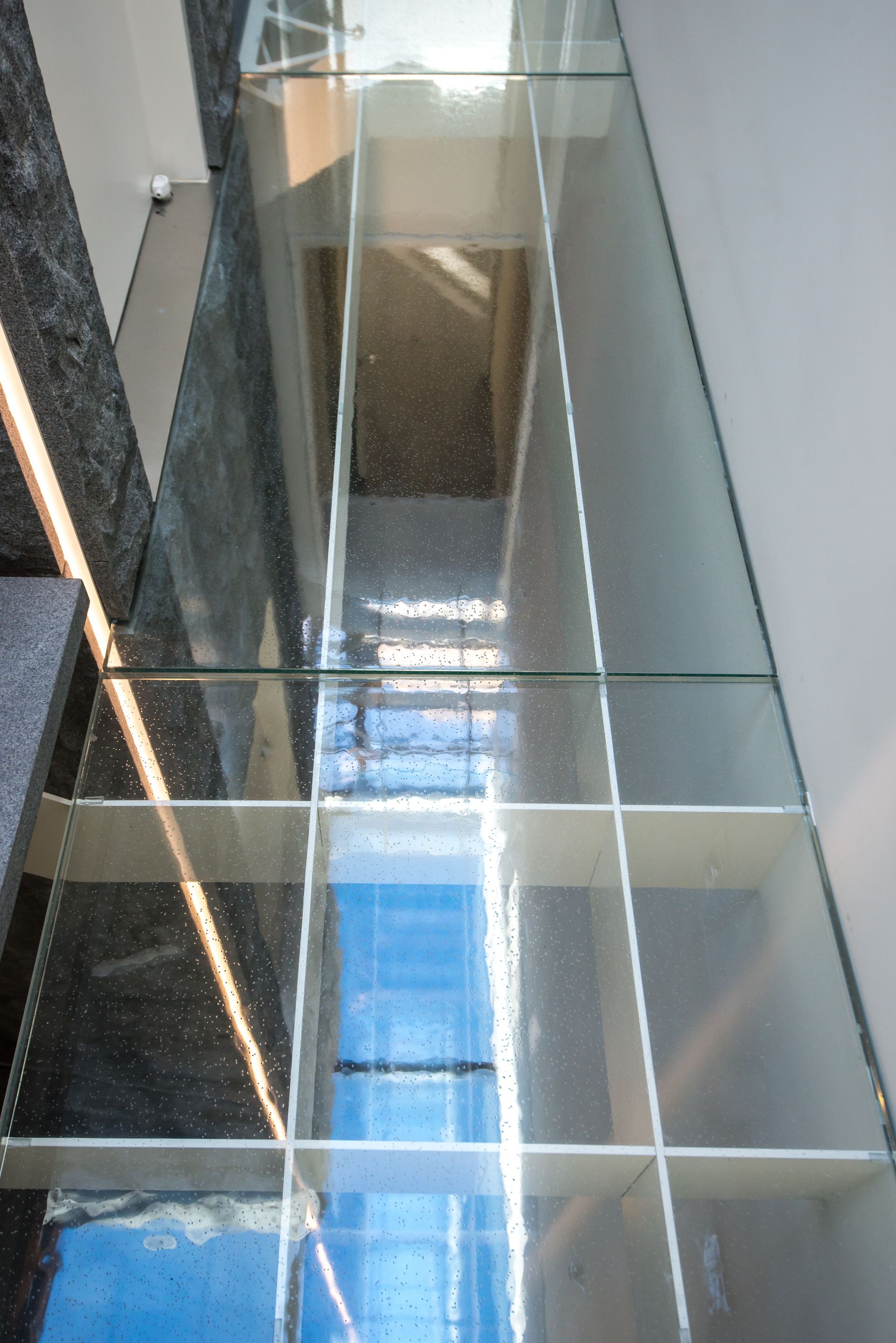 Modern staircase with glass railings and blue-tinted skylight above
