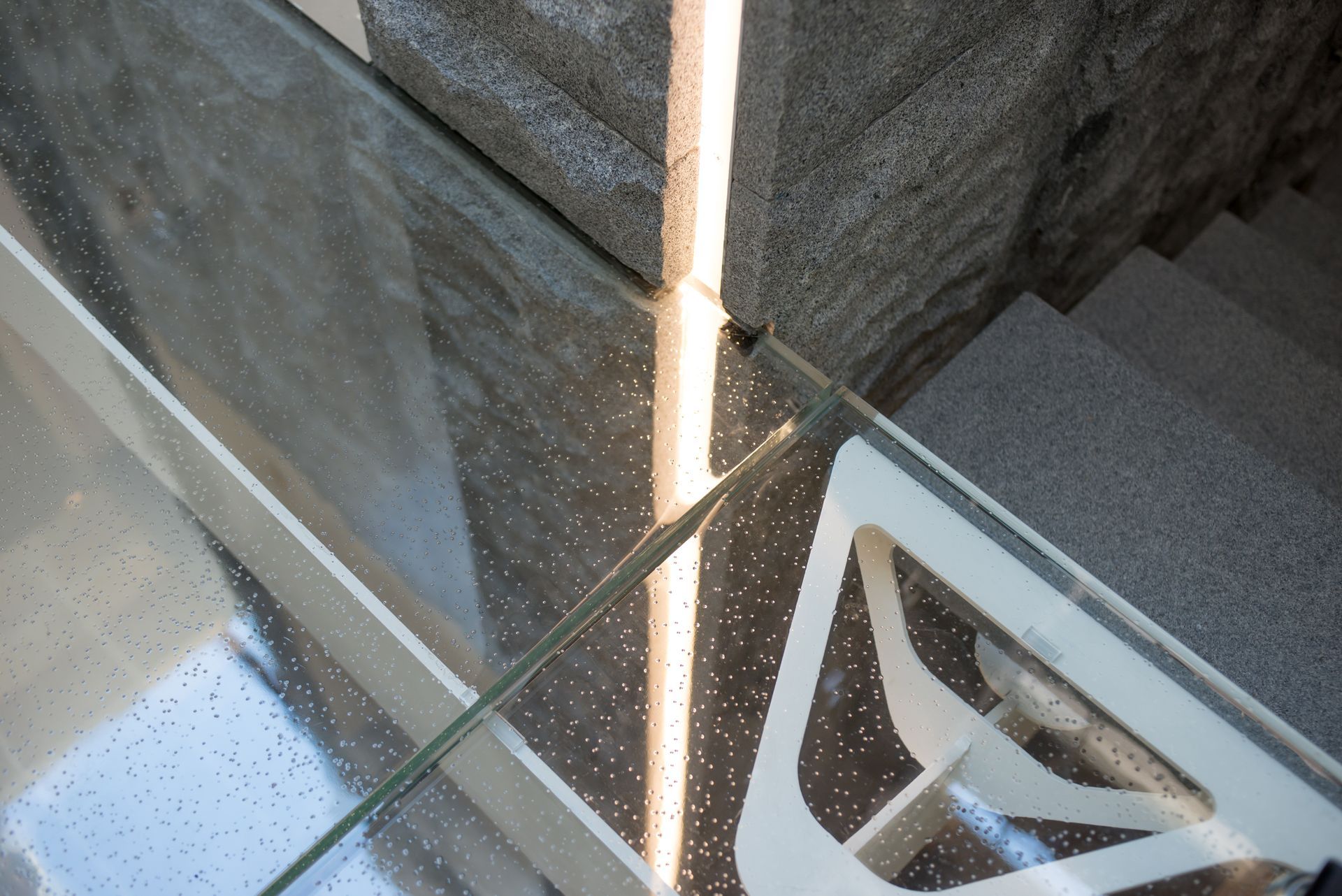 Glass railing beside stone steps with a vertical light reflection and a patterned floor below
