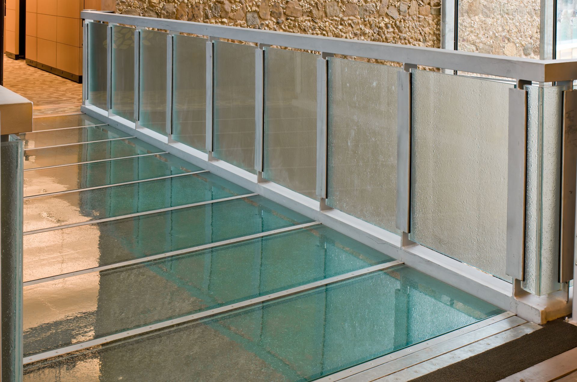 Glass-railed indoor stairway beside a turquoise pool or water feature