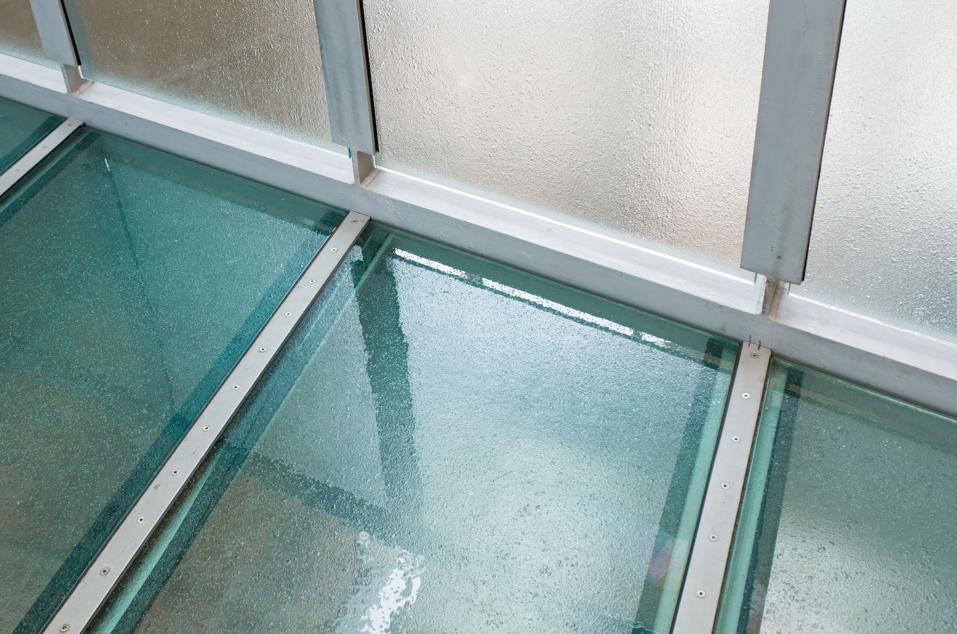 Textured glass skylight panes in a metal frame, with frosted windows and a teal floor reflection.