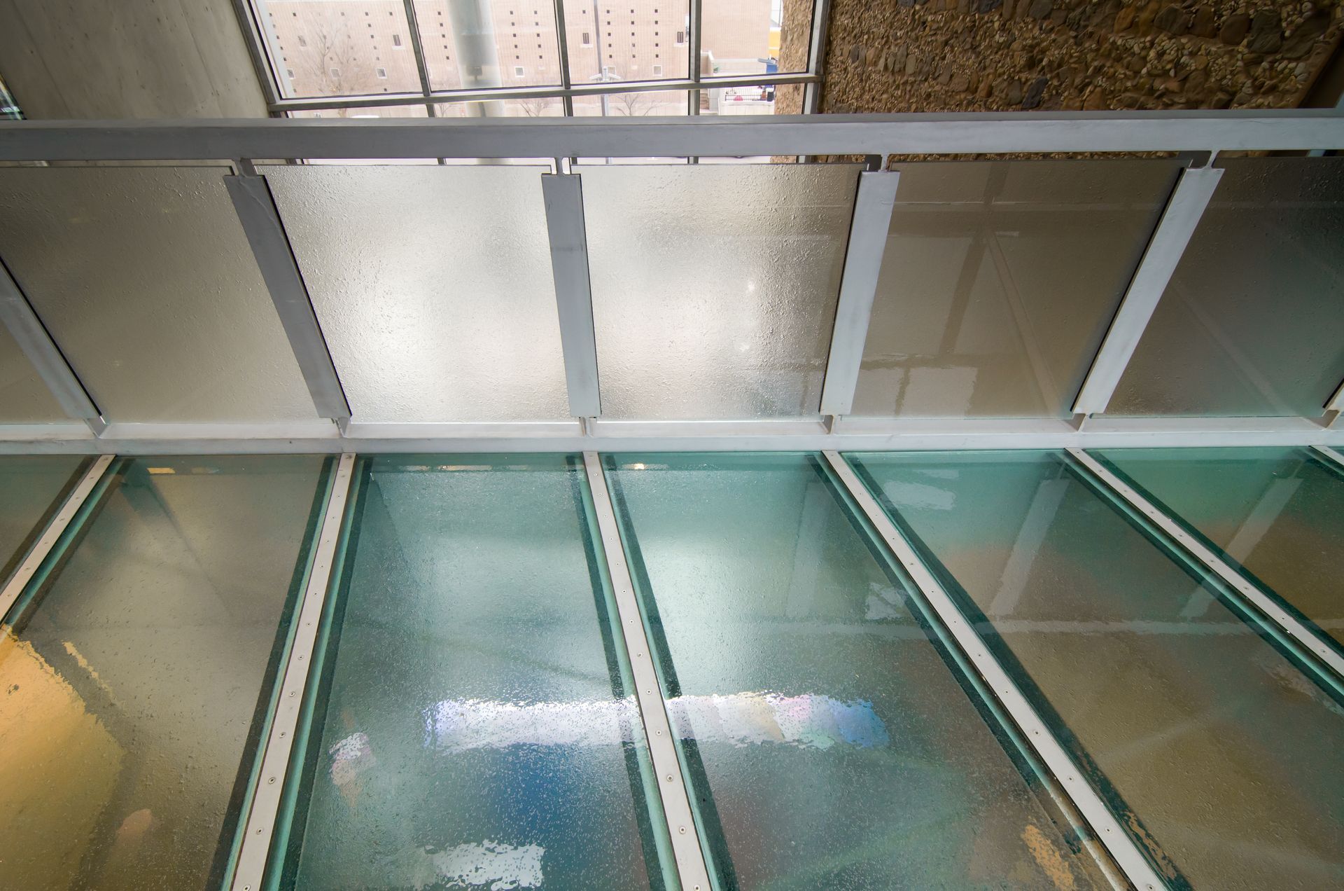 Glass-railed atrium with metal ceiling beams and skylights reflecting light on the floor