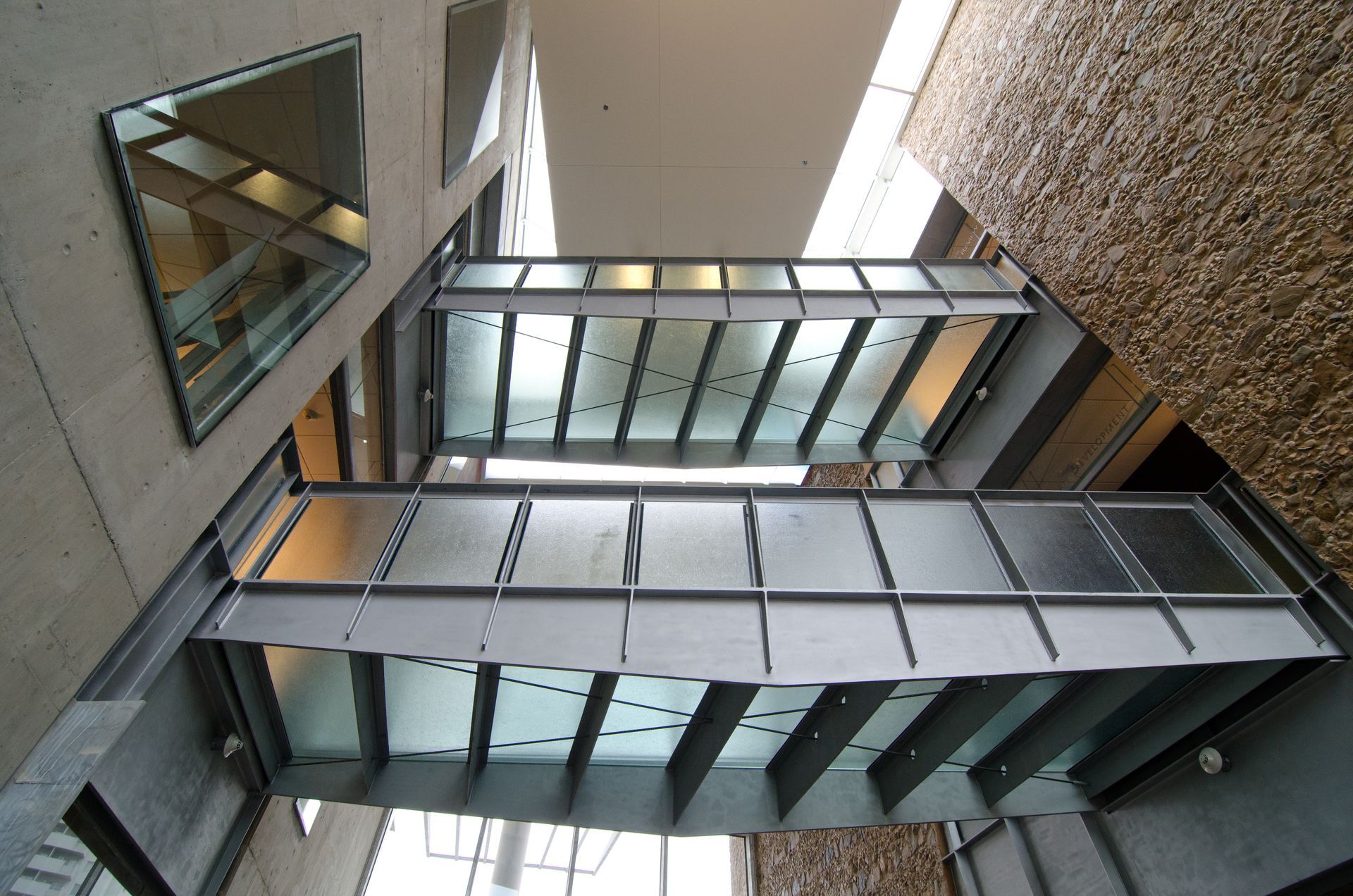 Modern glass-and-metal stairwell viewed upward between concrete walls