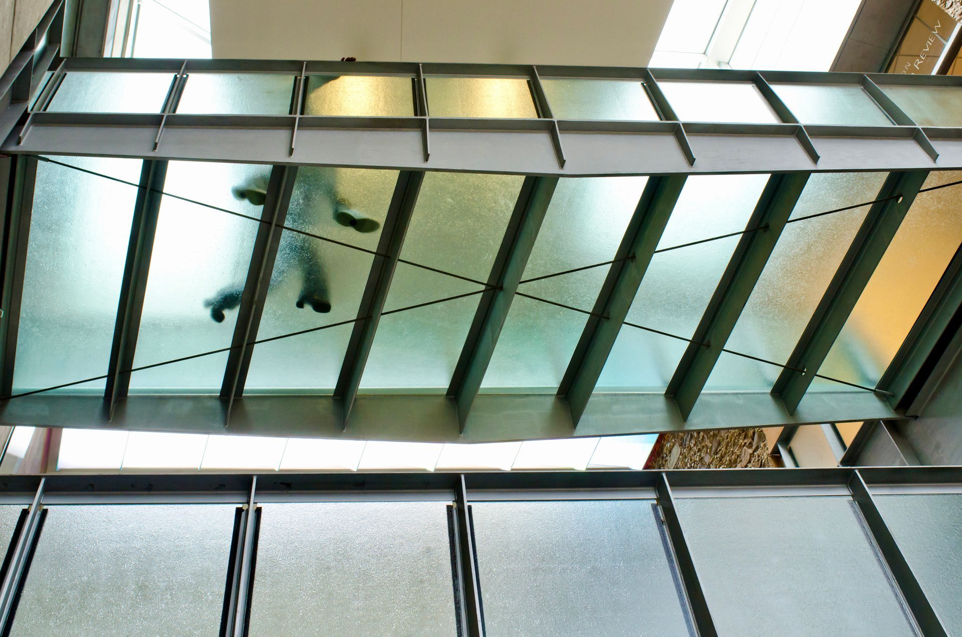 Glass-covered walkway with a person walking below seen through frosted panels