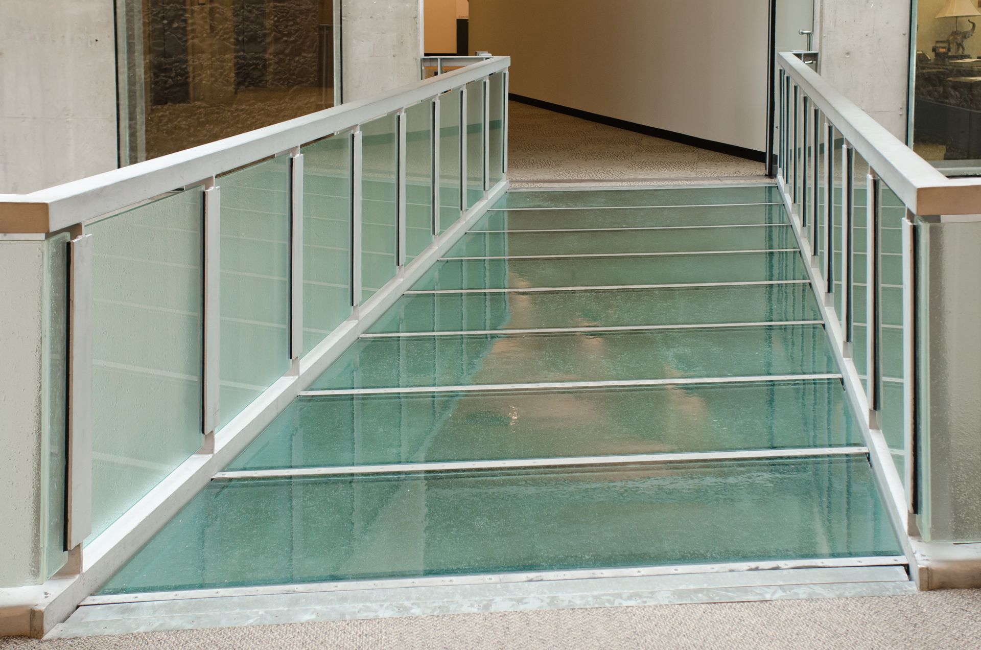 Glass-railed indoor ramp with green panels in a hallway