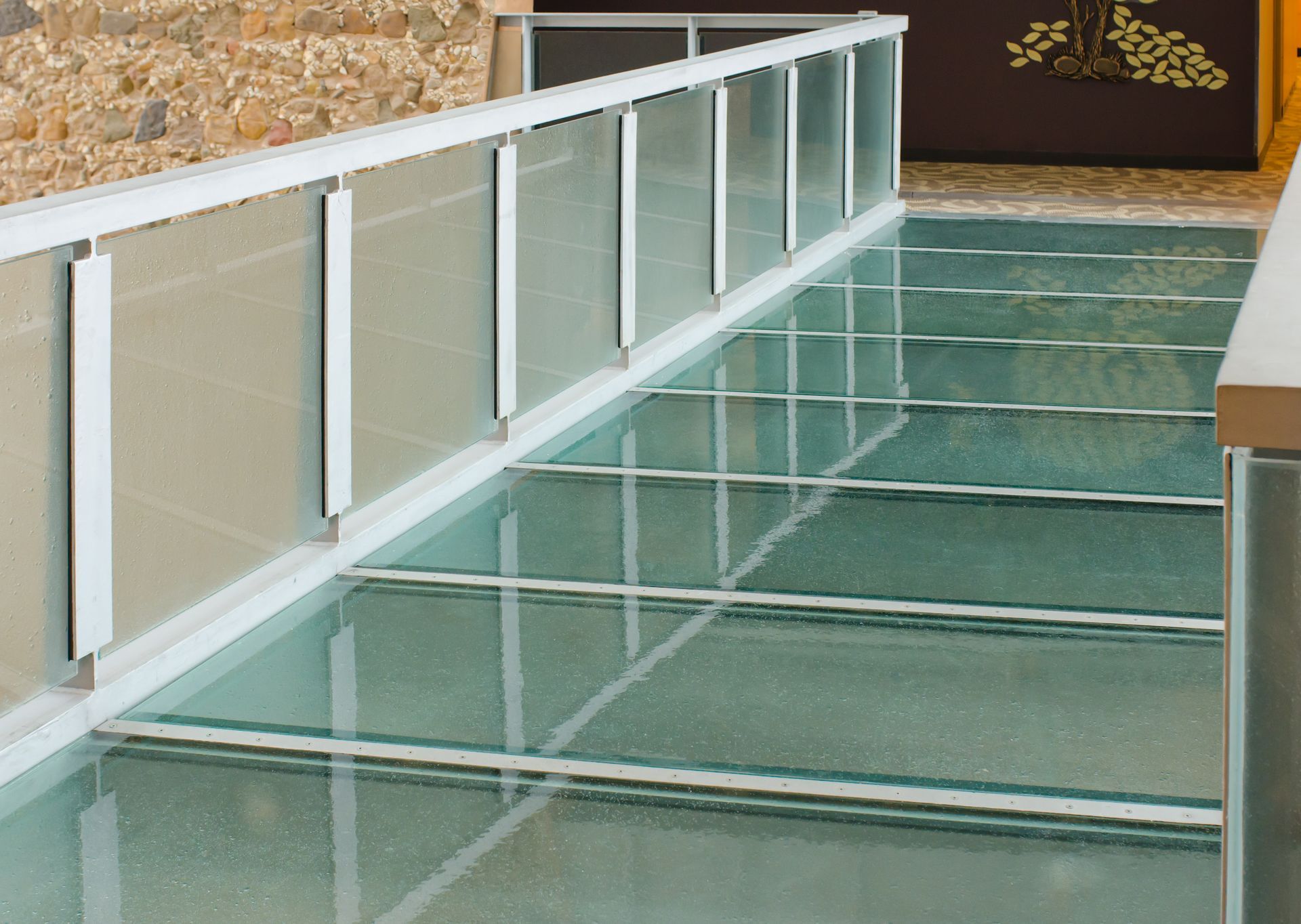 Glass-floor pedestrian bridge with white railings over water or a transparent channel