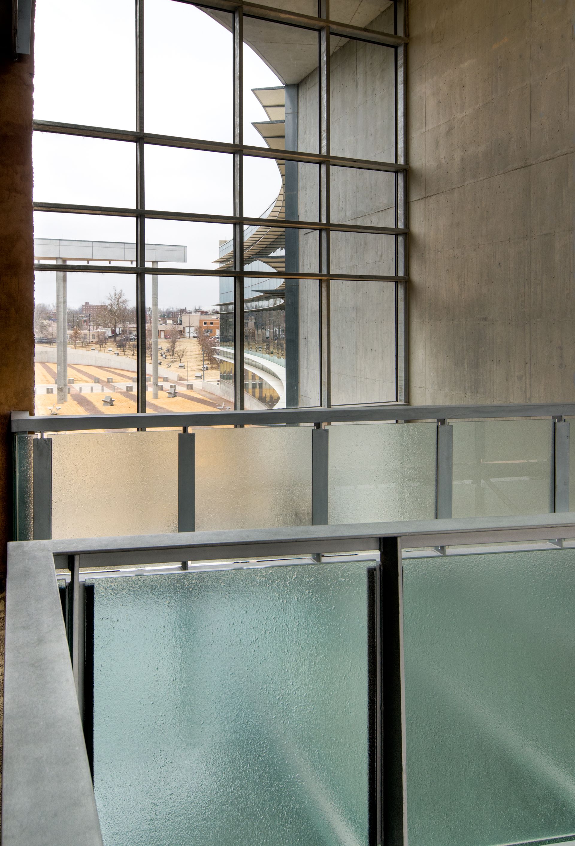 View from an indoor balcony with frosted glass railing and a large window overlooking a city street.