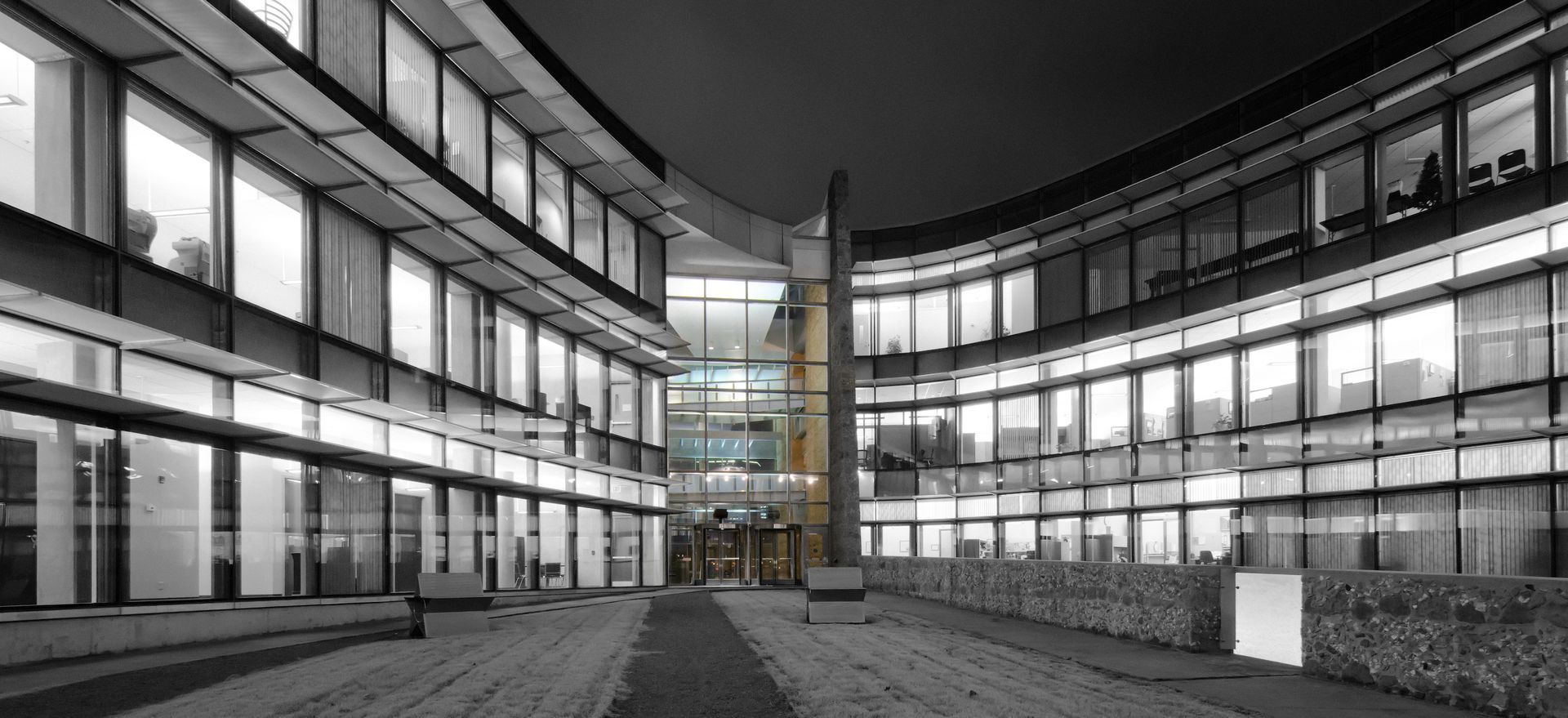 Modern glass office courtyard at night with lit windows and a central tower