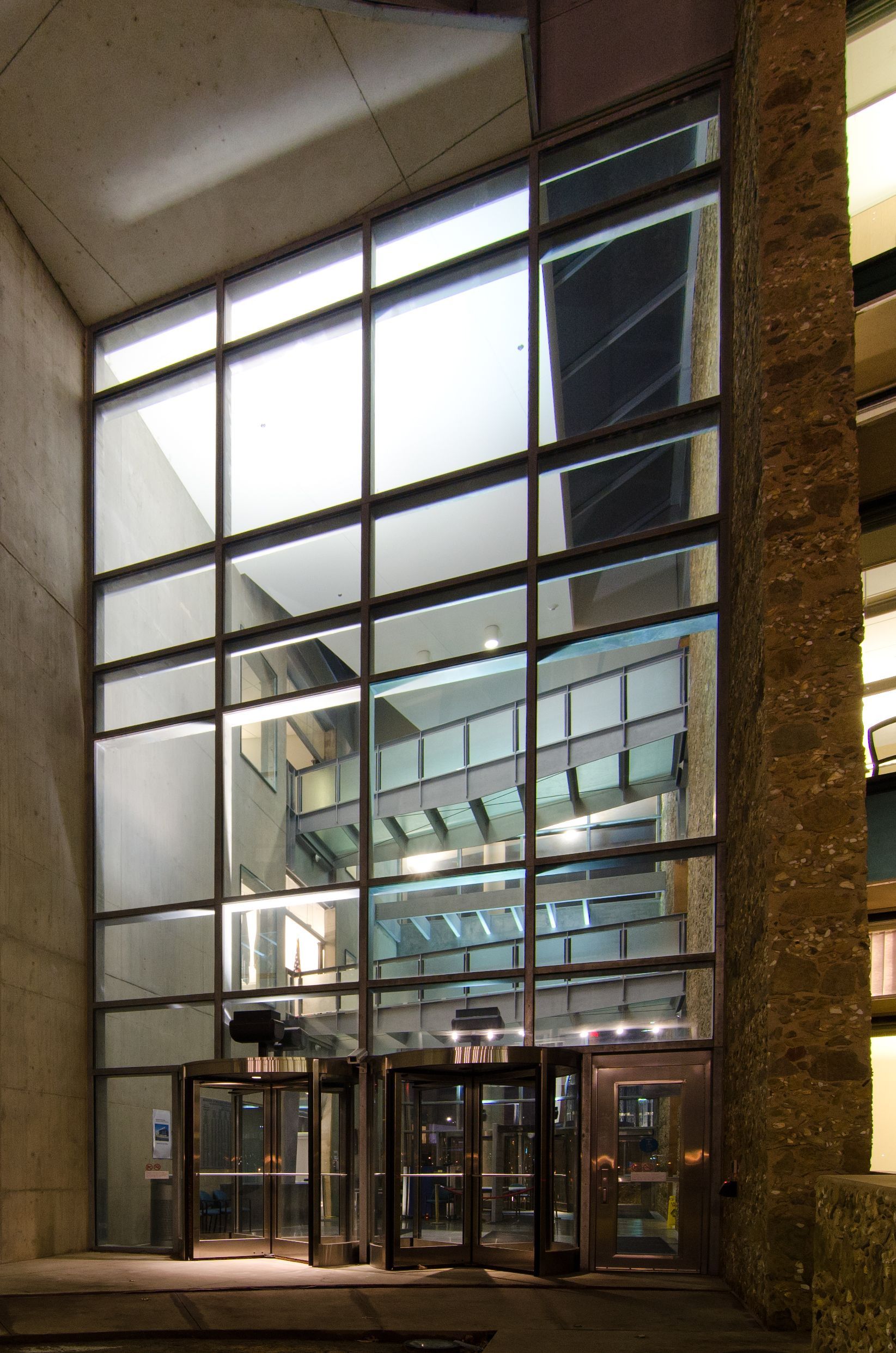 Glass-front office building entrance at night with revolving doors and bright interior lights