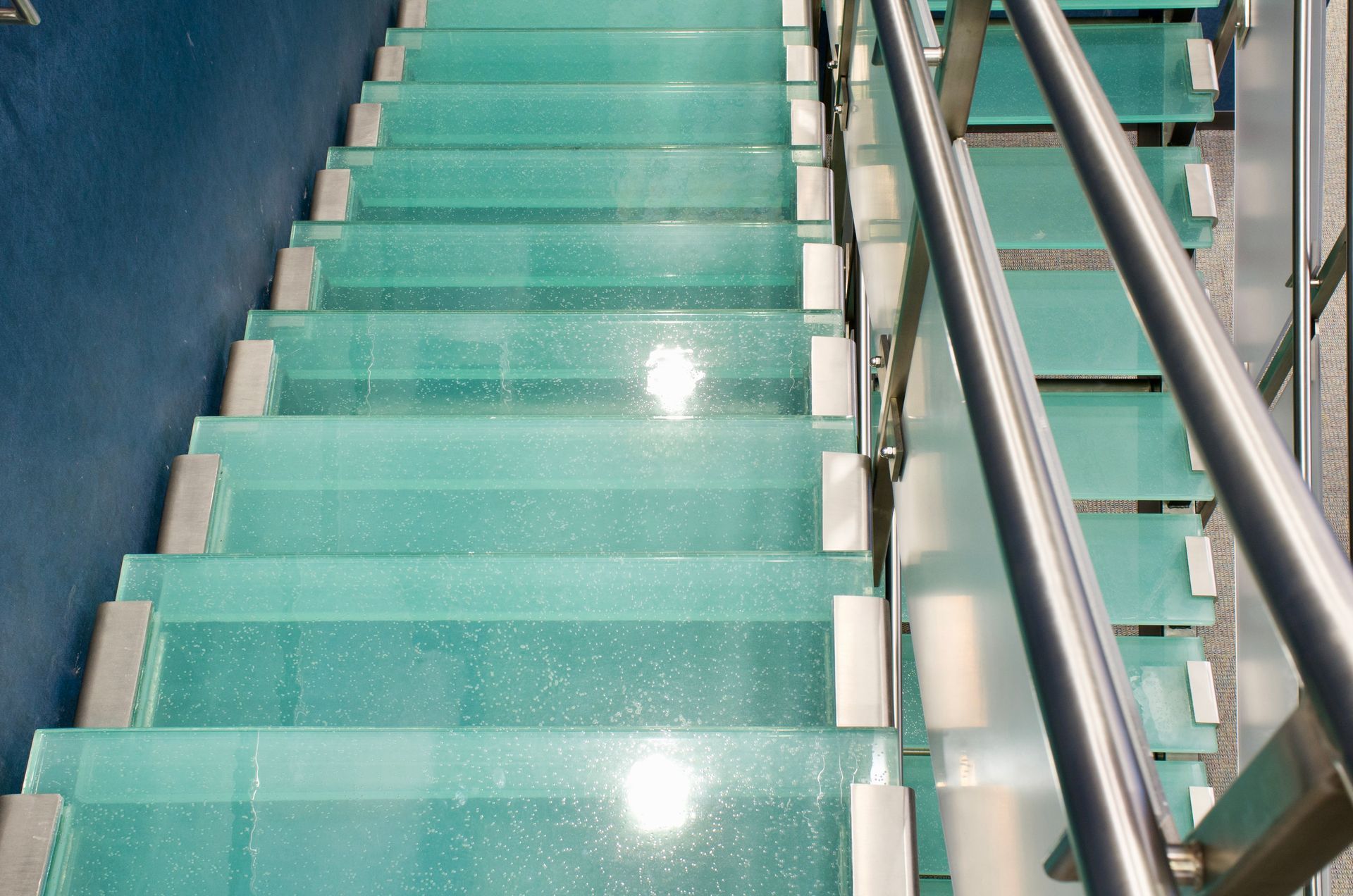 Green-tiled staircase with metal handrails and blue walls, viewed from above