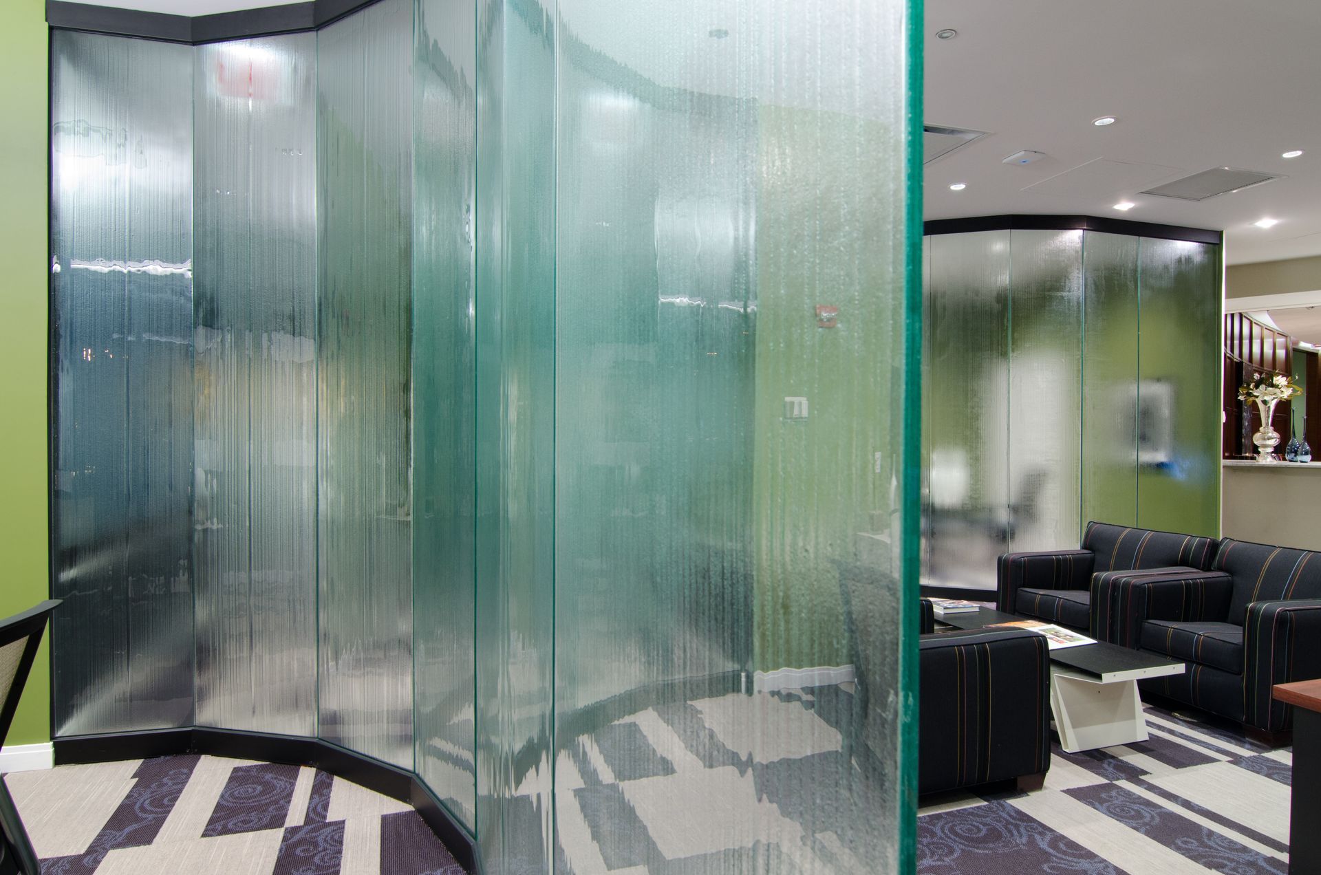 Modern lounge with curved frosted glass partitions and black seating under bright ceiling lights