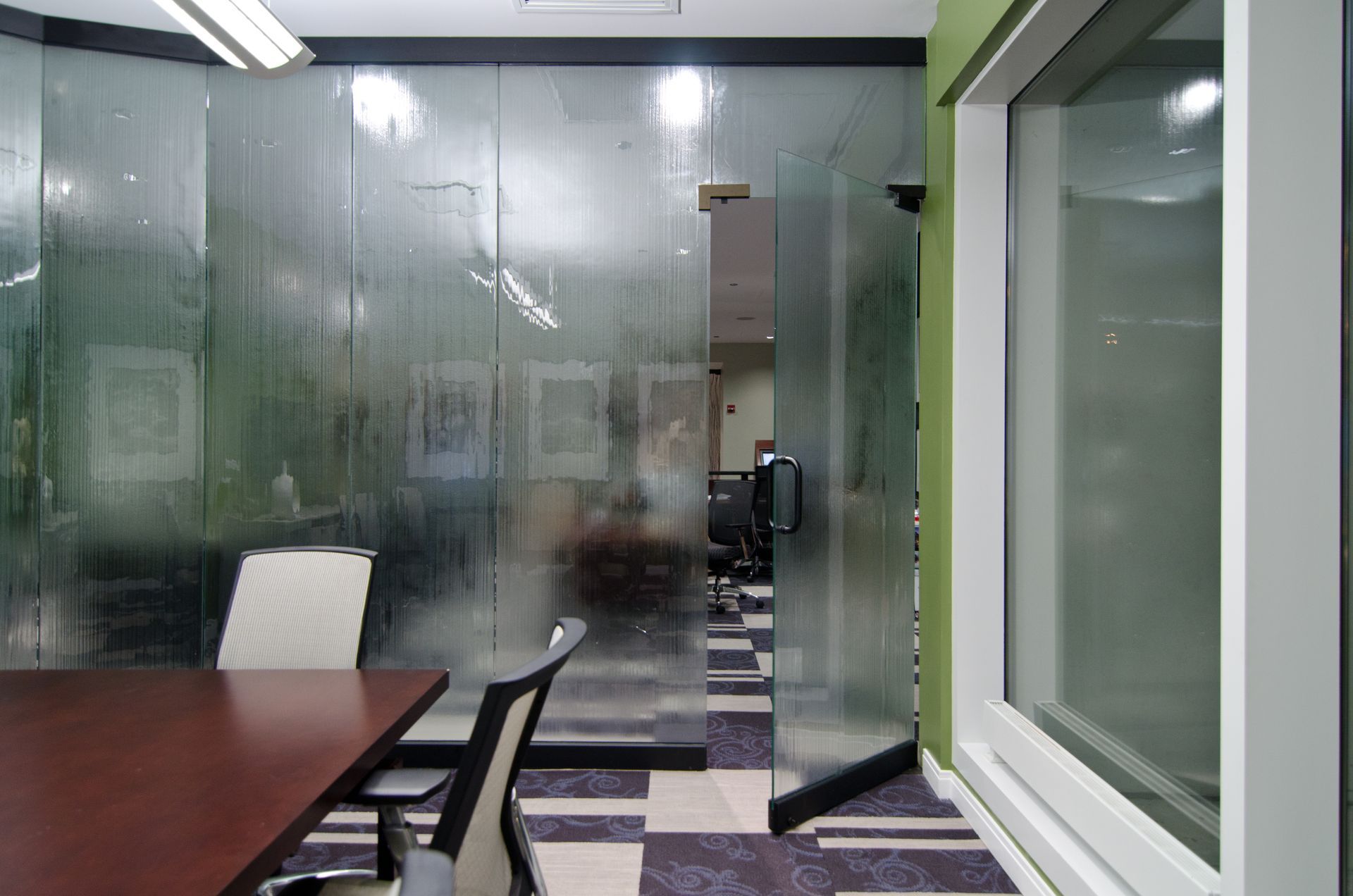 Modern office conference room with glass walls, dark table, and patterned carpet