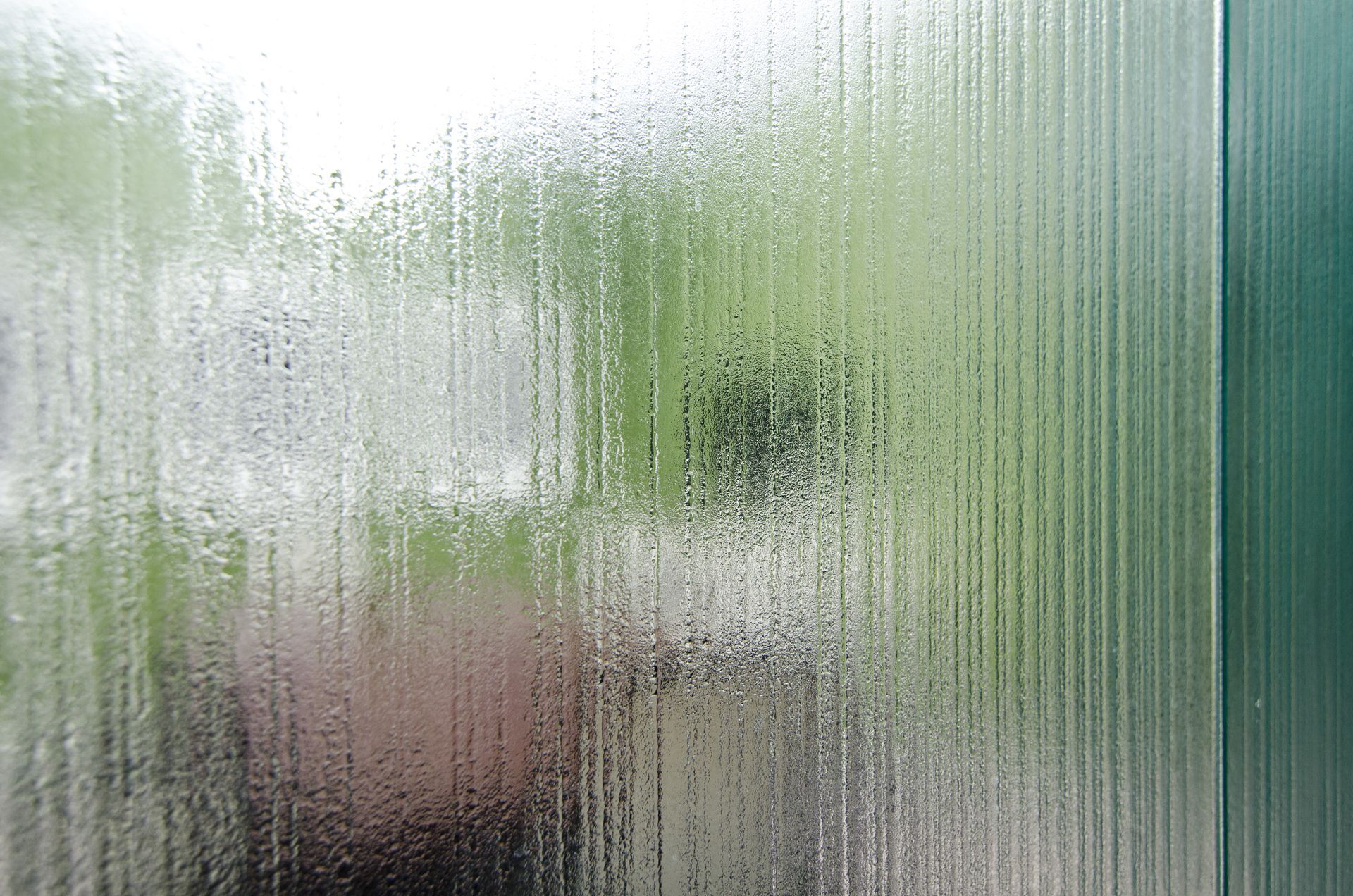 Blurred view through a frosted glass window, with green foliage and a pink planter outside.