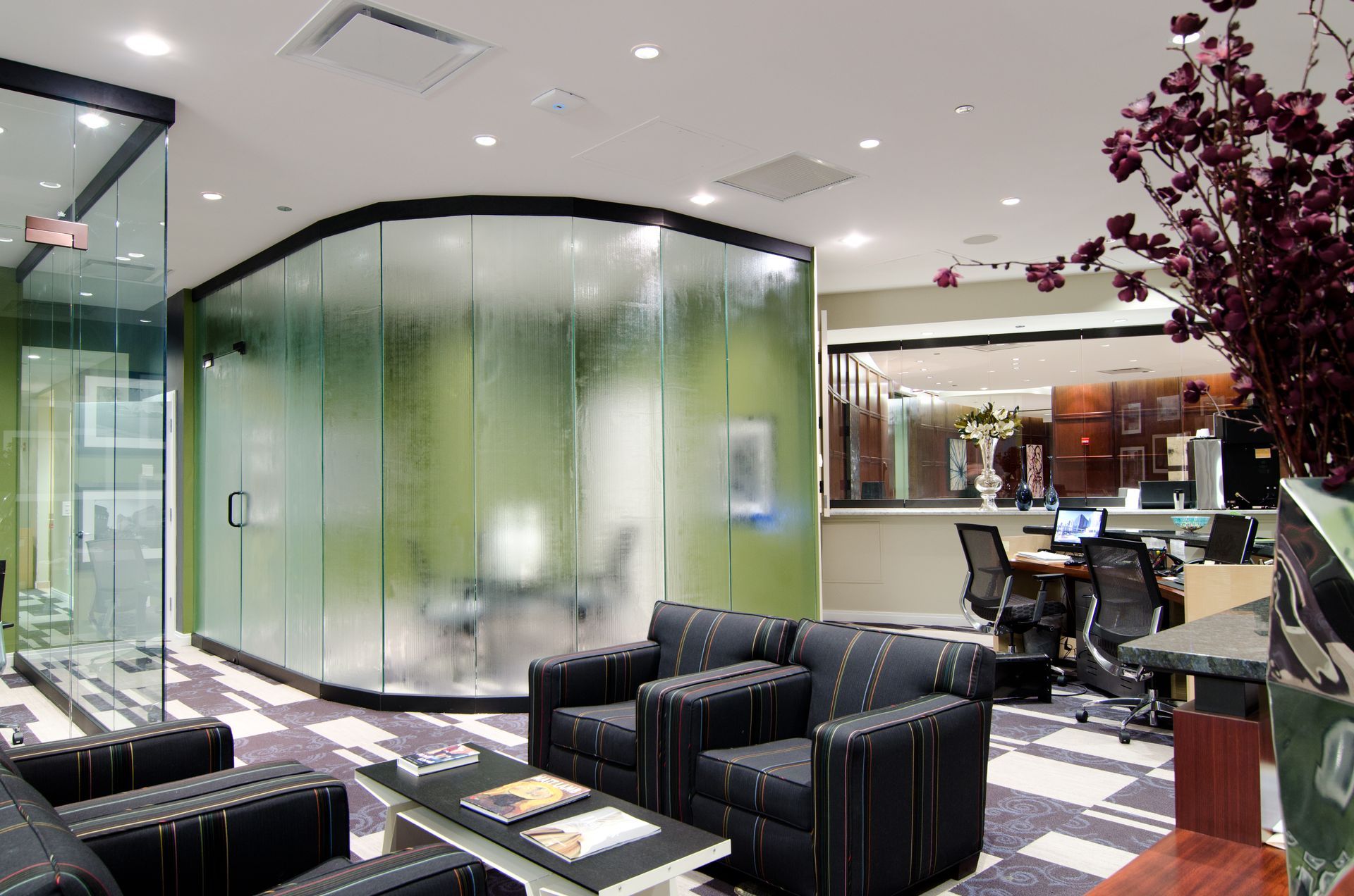 Modern office lobby with glass meeting pod, black chairs, and patterned carpet