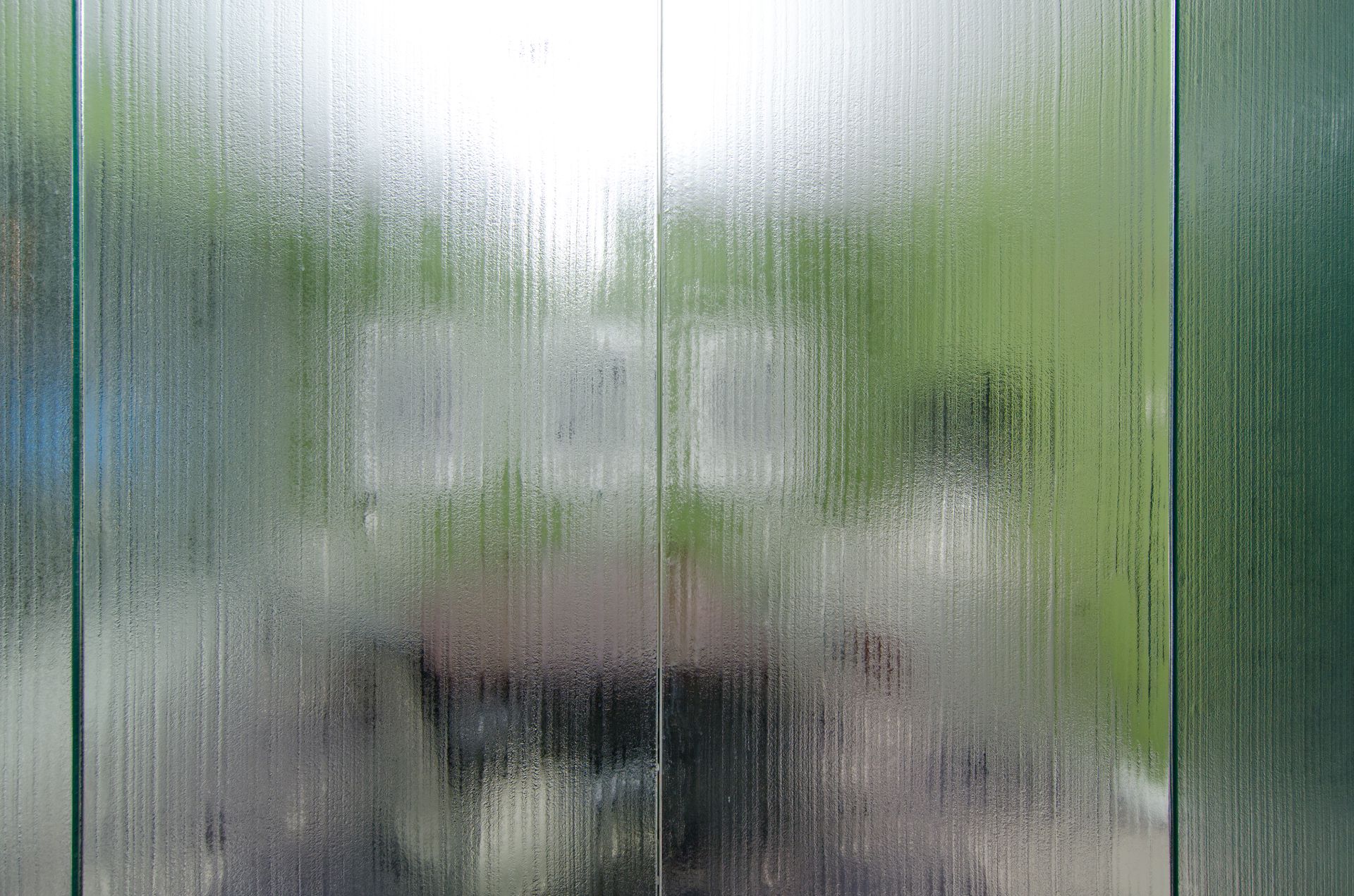Blurred view through frosted glass of a patio with chairs and green trees beyond.