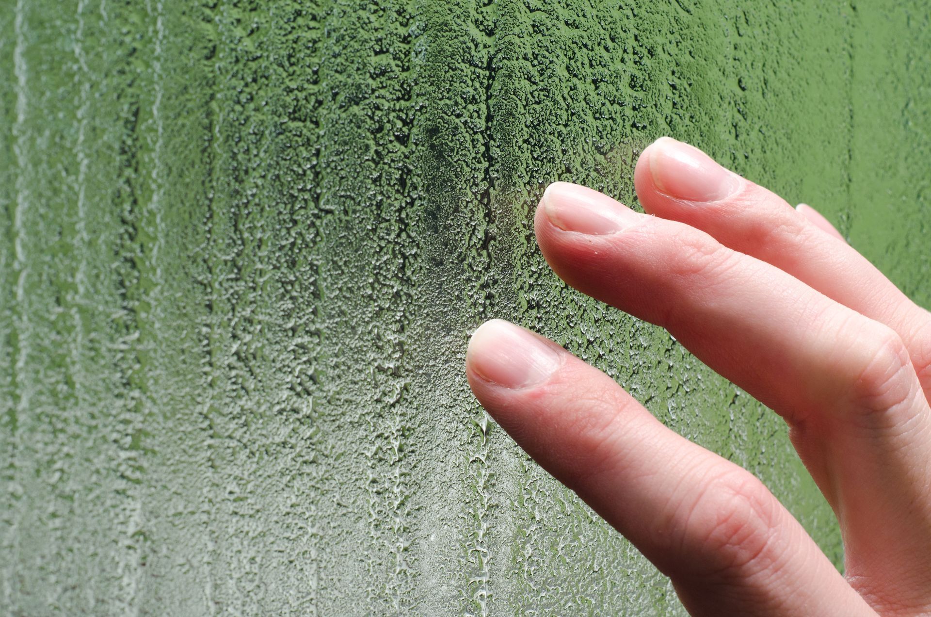 Hand touching fogged glass with water droplets and a green background