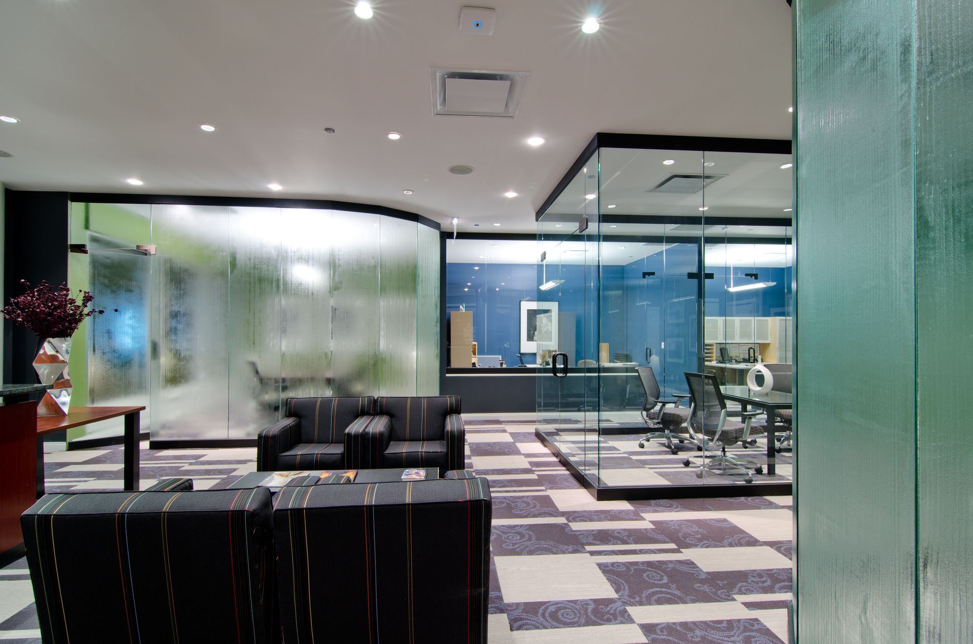 Modern office lobby with black chairs, glass walls, and patterned carpet in a bright reception area