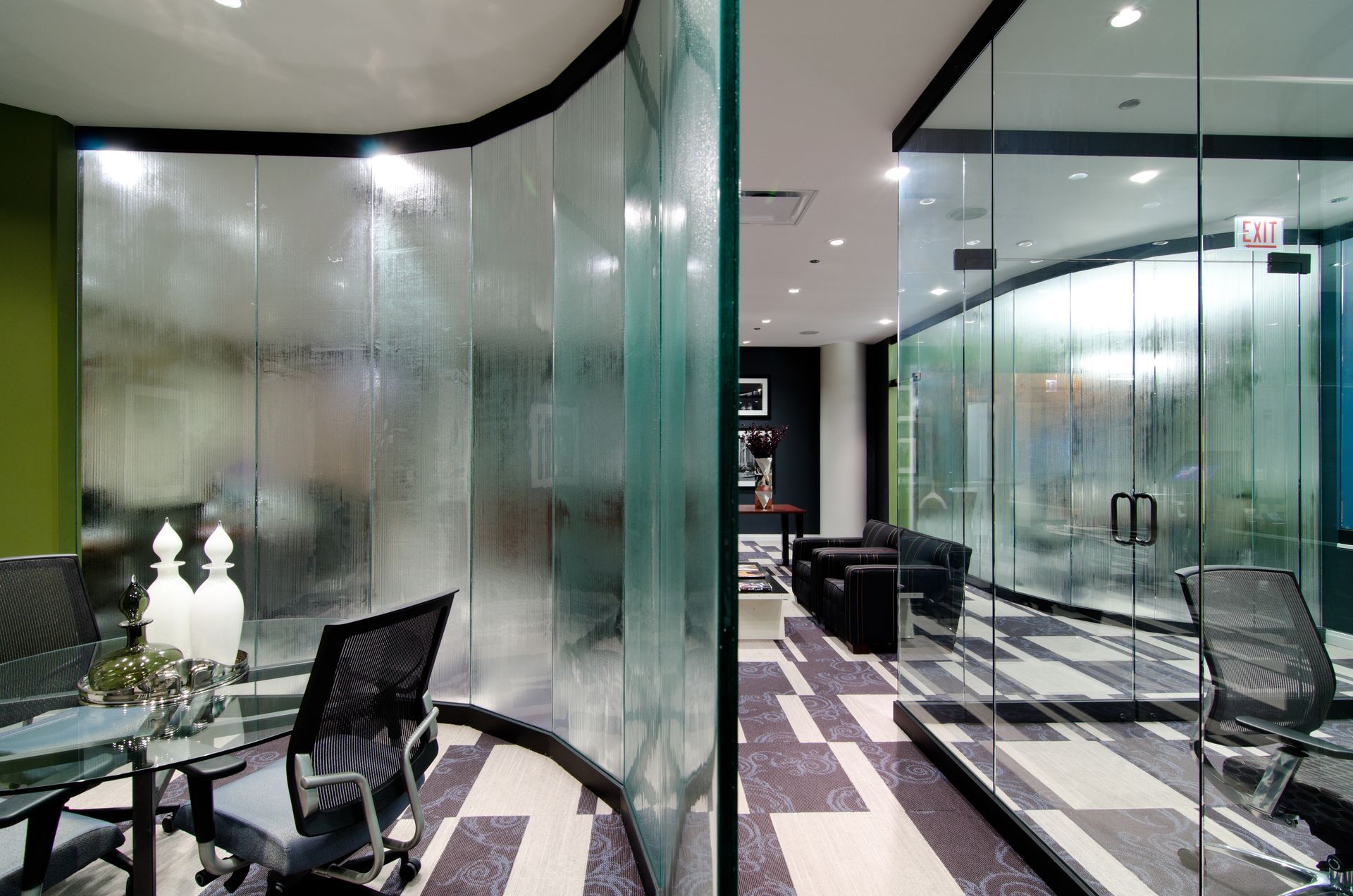 Modern office lounge with frosted glass walls, black chairs, and a purple-patterned carpet corridor