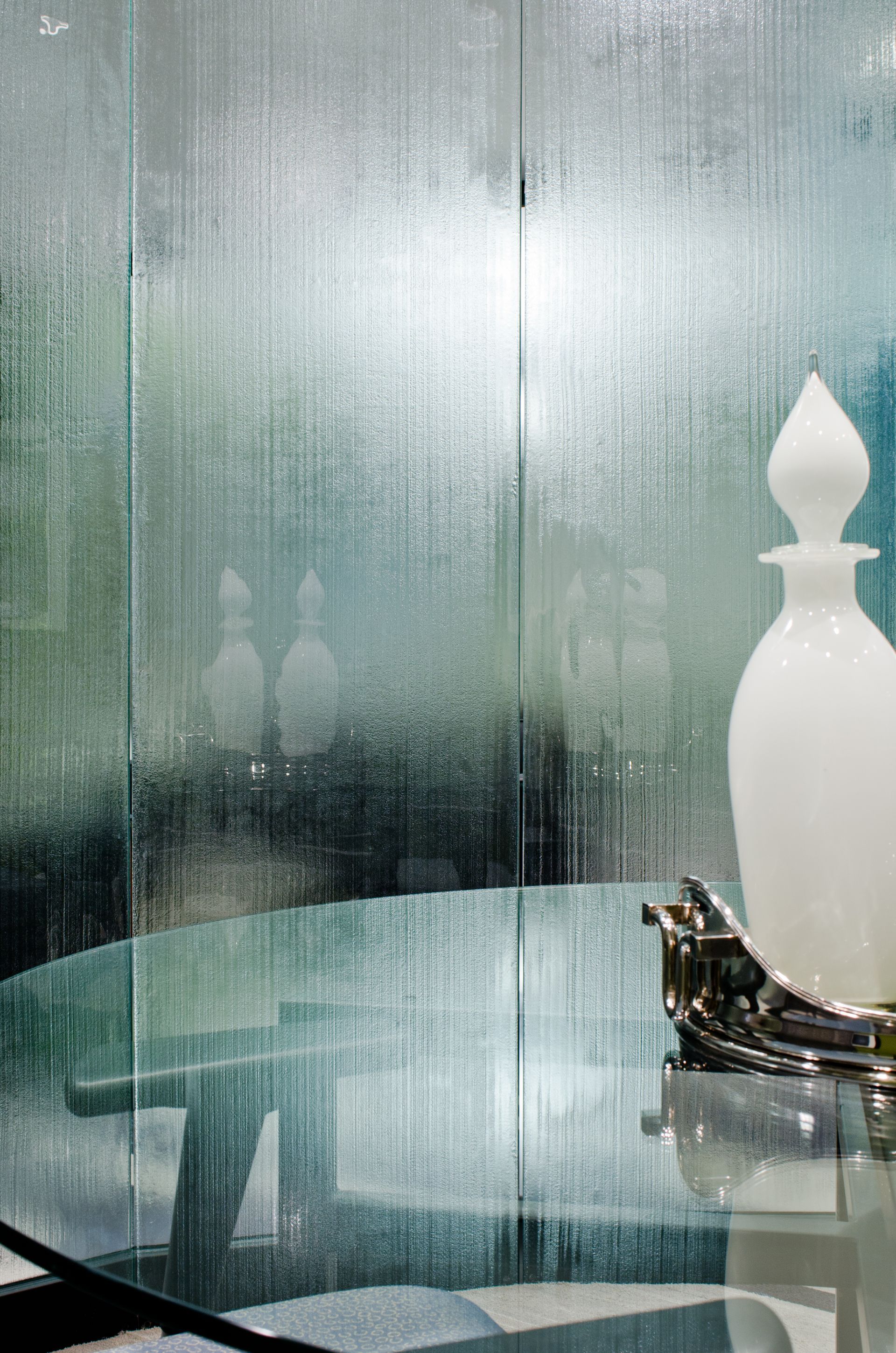 Glass table with white decorative vase beside a frosted glass wall