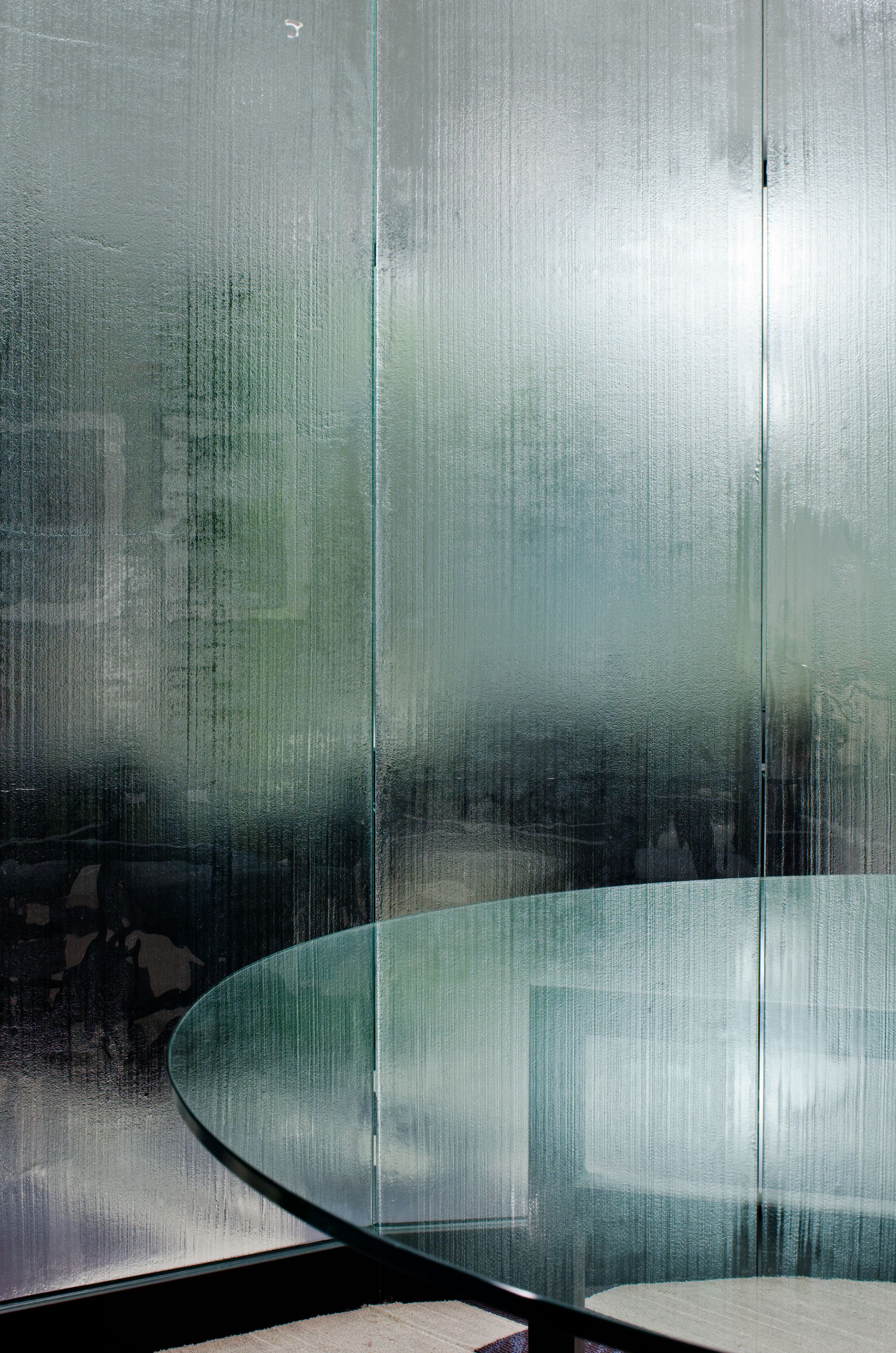 Rain-streaked glass with a modern glass table in front of a blurred green-gray background