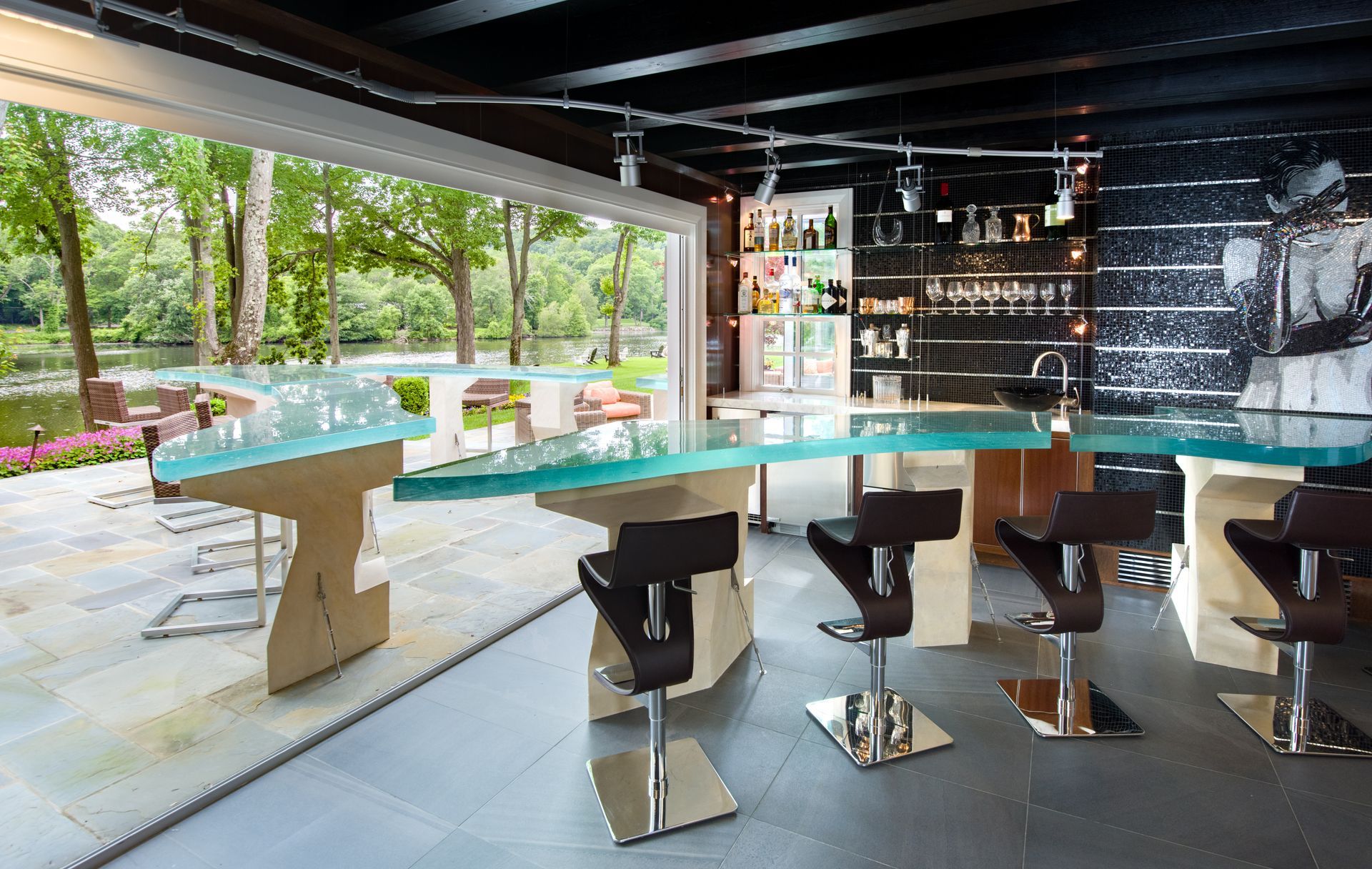 Modern bar with glass counter, designer stools, and open terrace view of a green garden