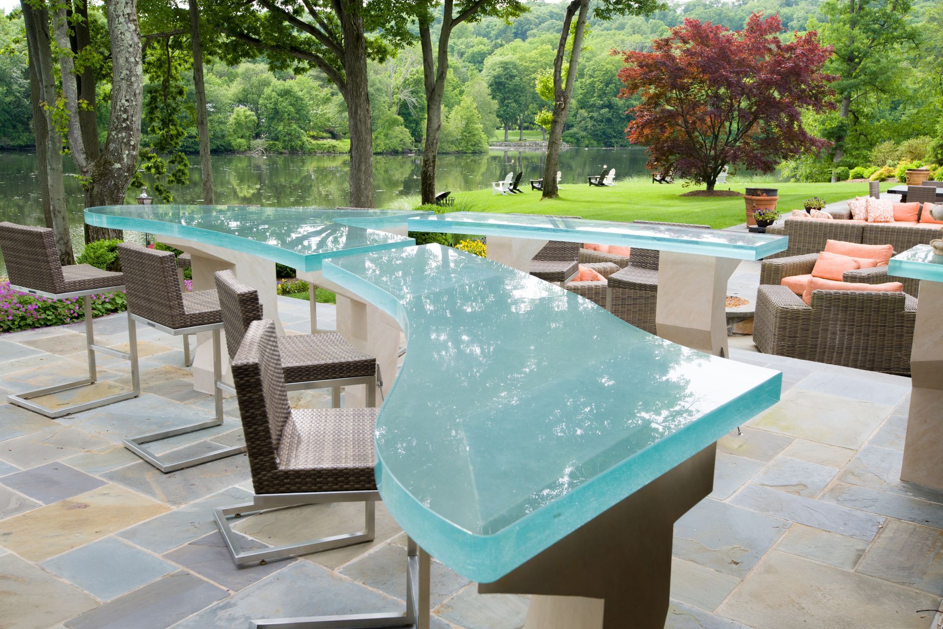 Outdoor patio with a turquoise glass table, wicker chairs, and a garden view