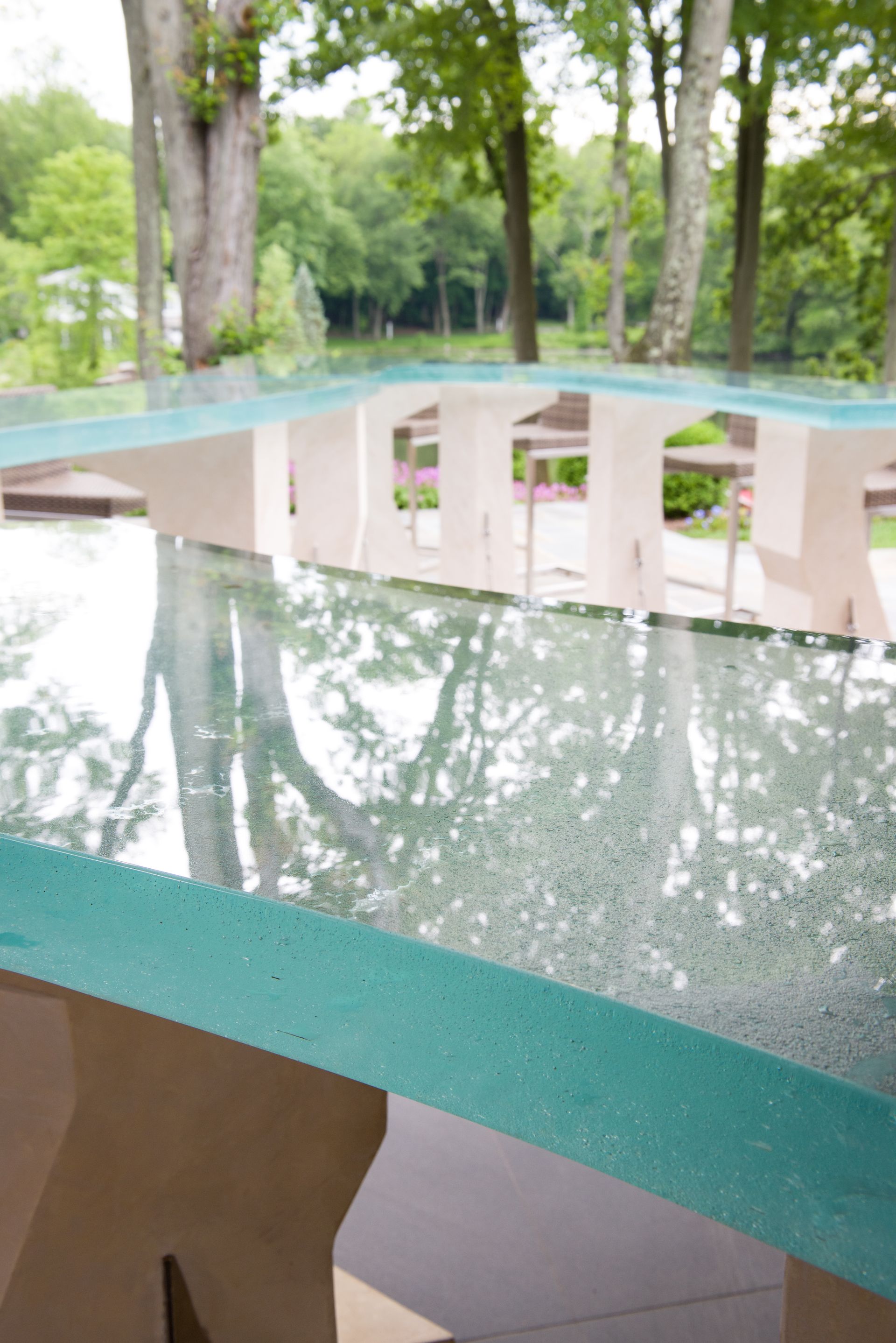 Turquoise glass railing reflecting trees in a park-like outdoor setting