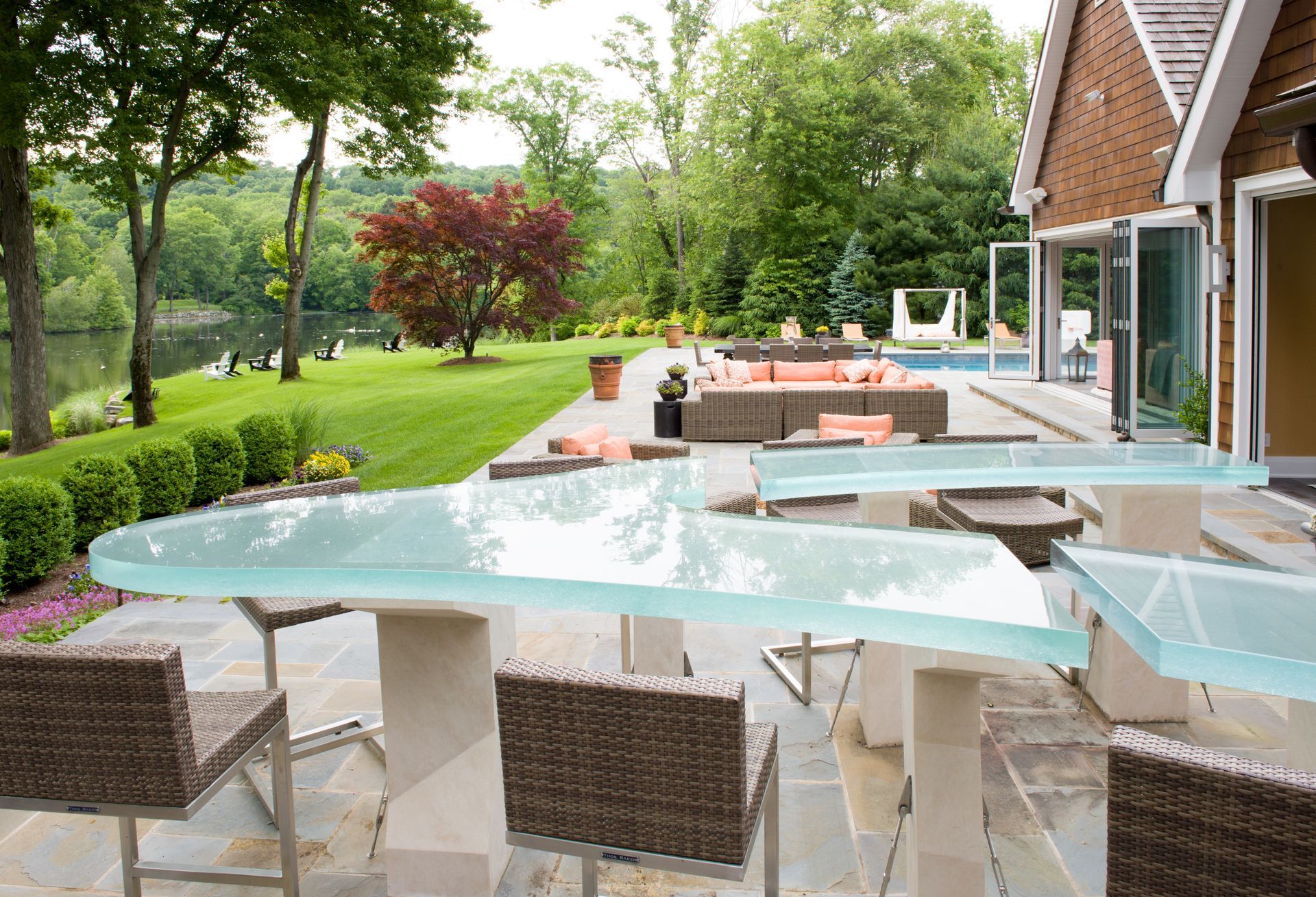 Outdoor patio with glass dining table, wicker chairs, and a lounge area beside a green backyard and pool