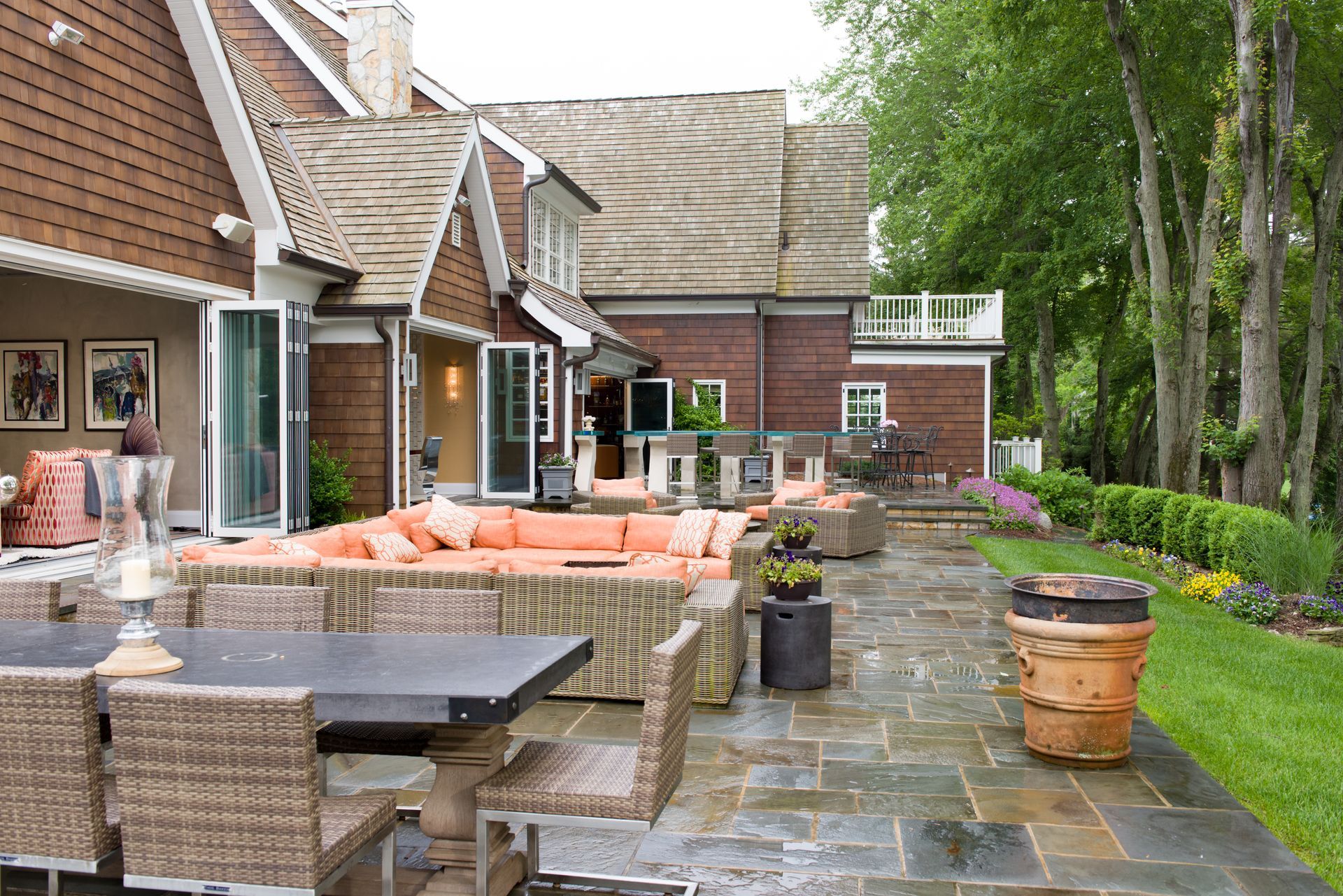 Backyard patio with wicker seating, orange cushions, and a stone walkway beside a house and garden