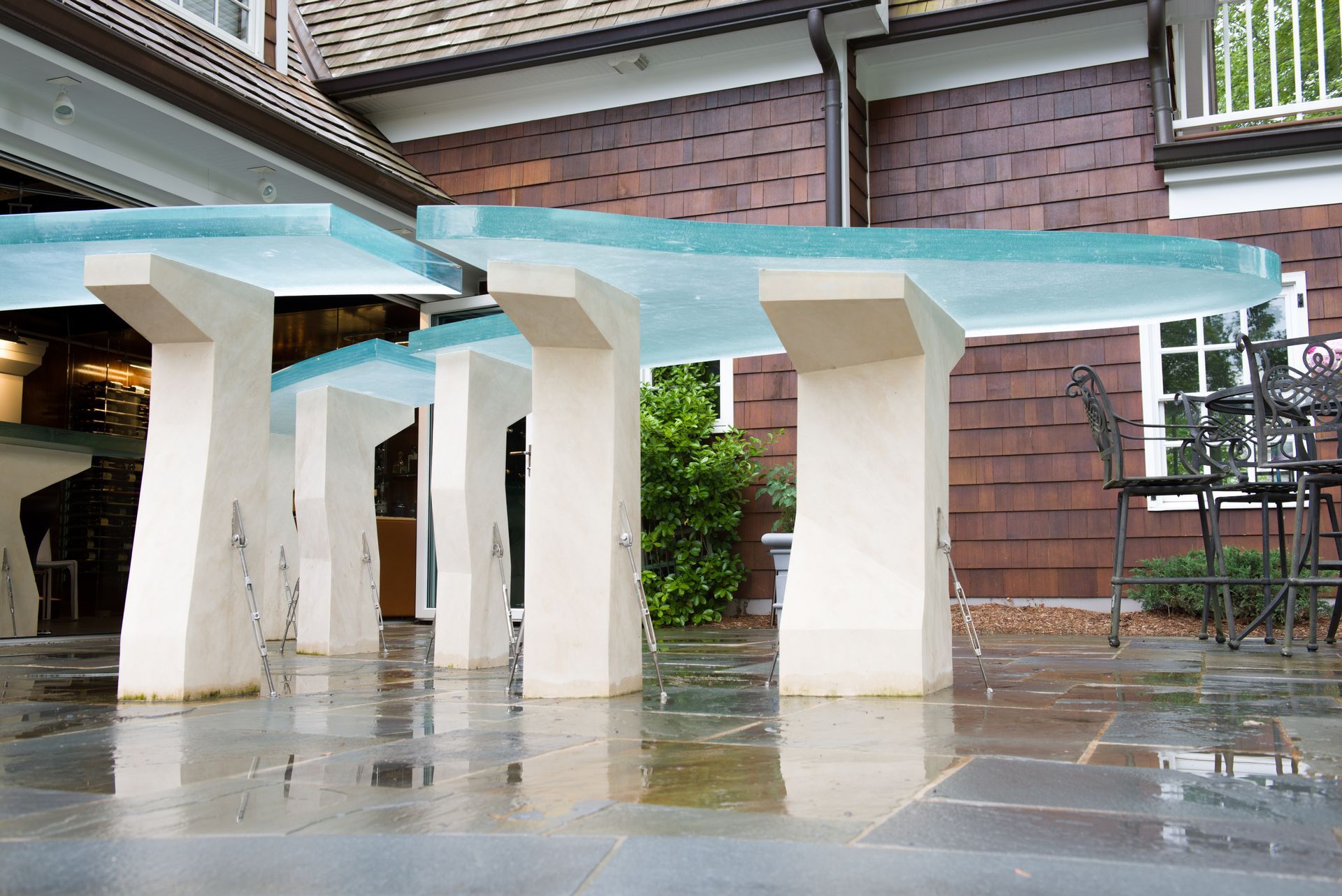 Modern covered walkway with turquoise roof, white pillars, and wet pavement outside a brick building