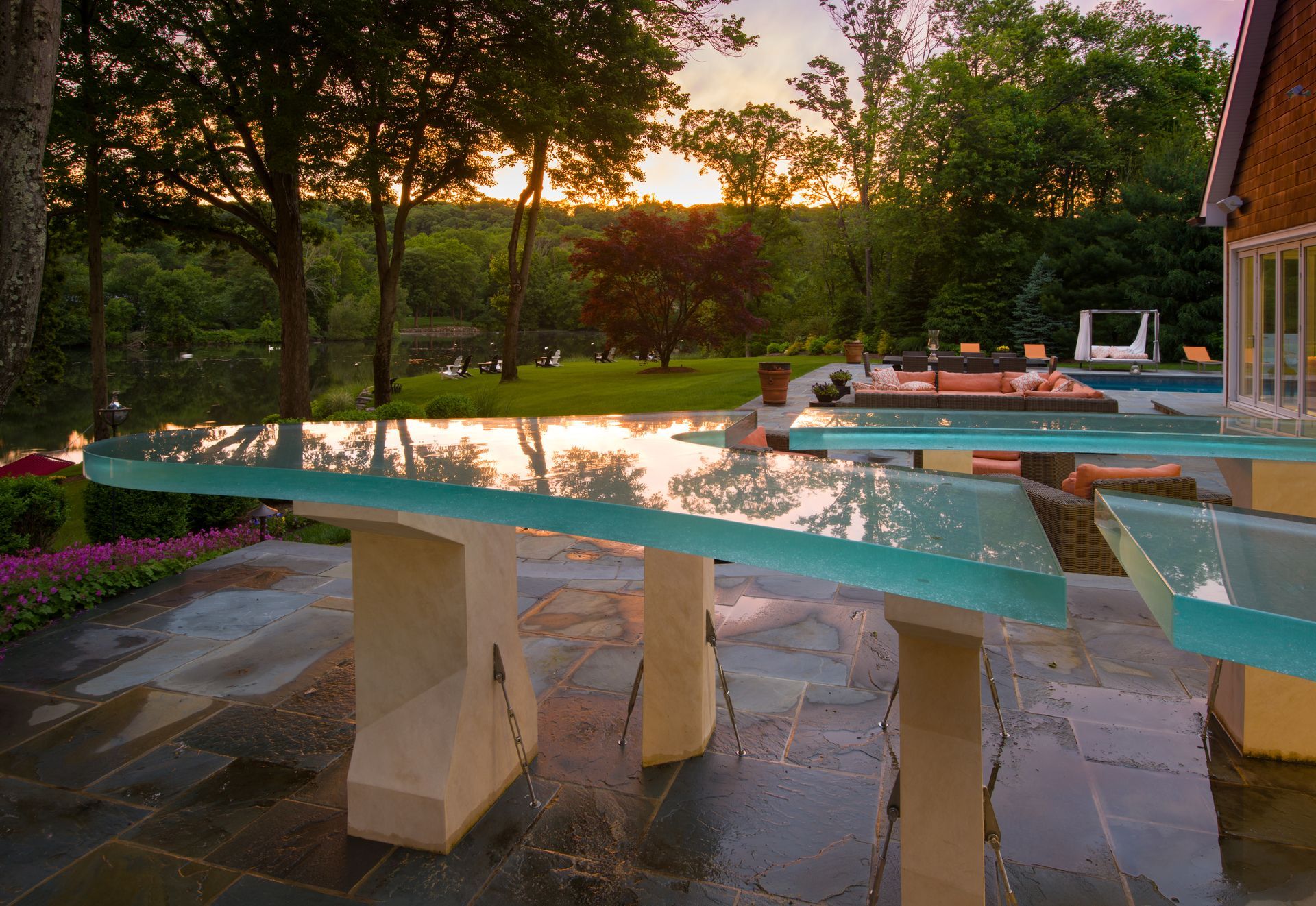Backyard pool at sunset with a stone diving board and patio beside a house
