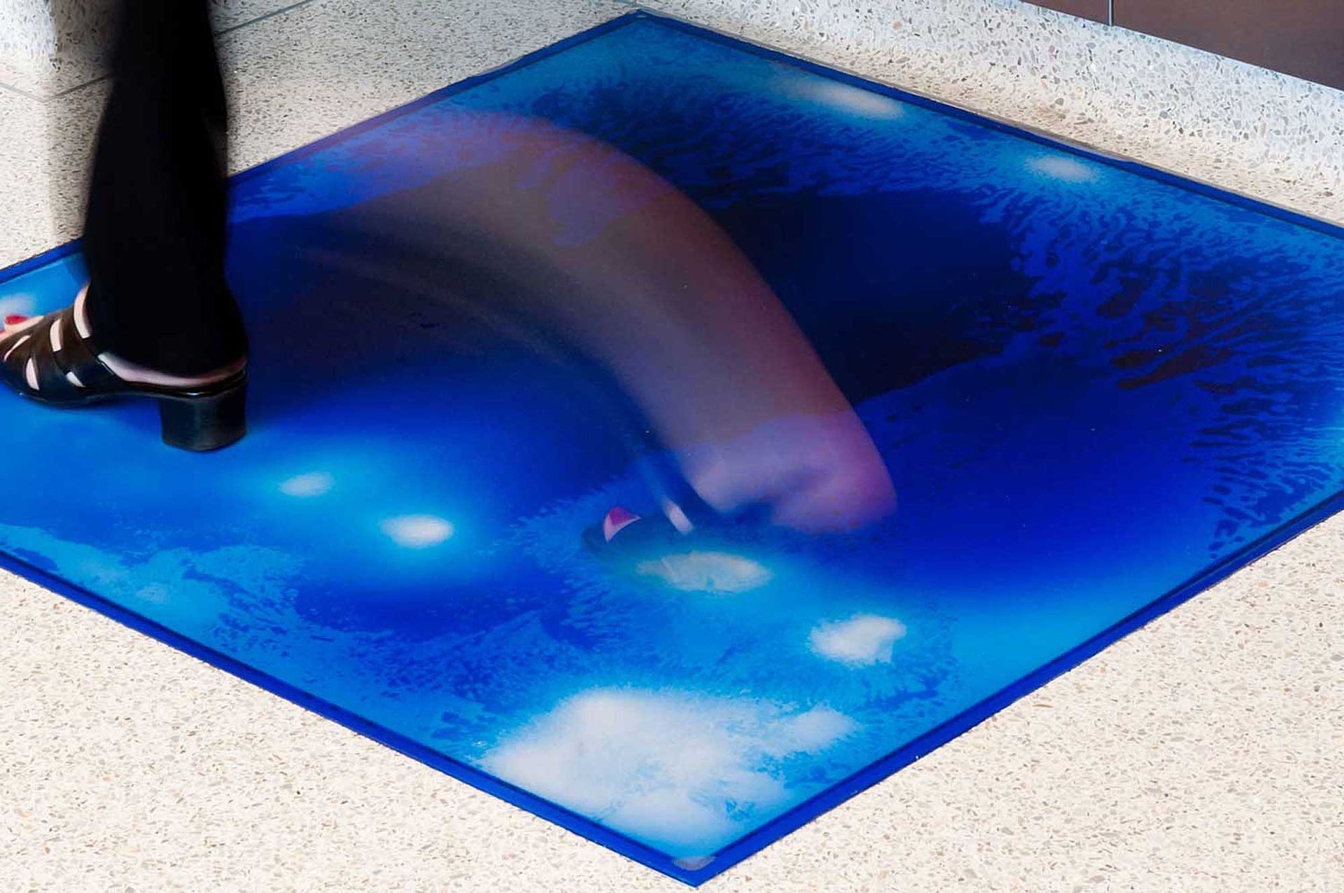 A hand spreading blue paint on paper with a brush, creating a glossy abstract swath.