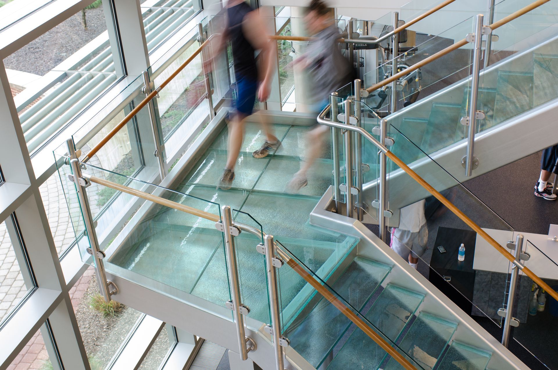 Blurred people walking on a glass staircase with metal railings in a modern building