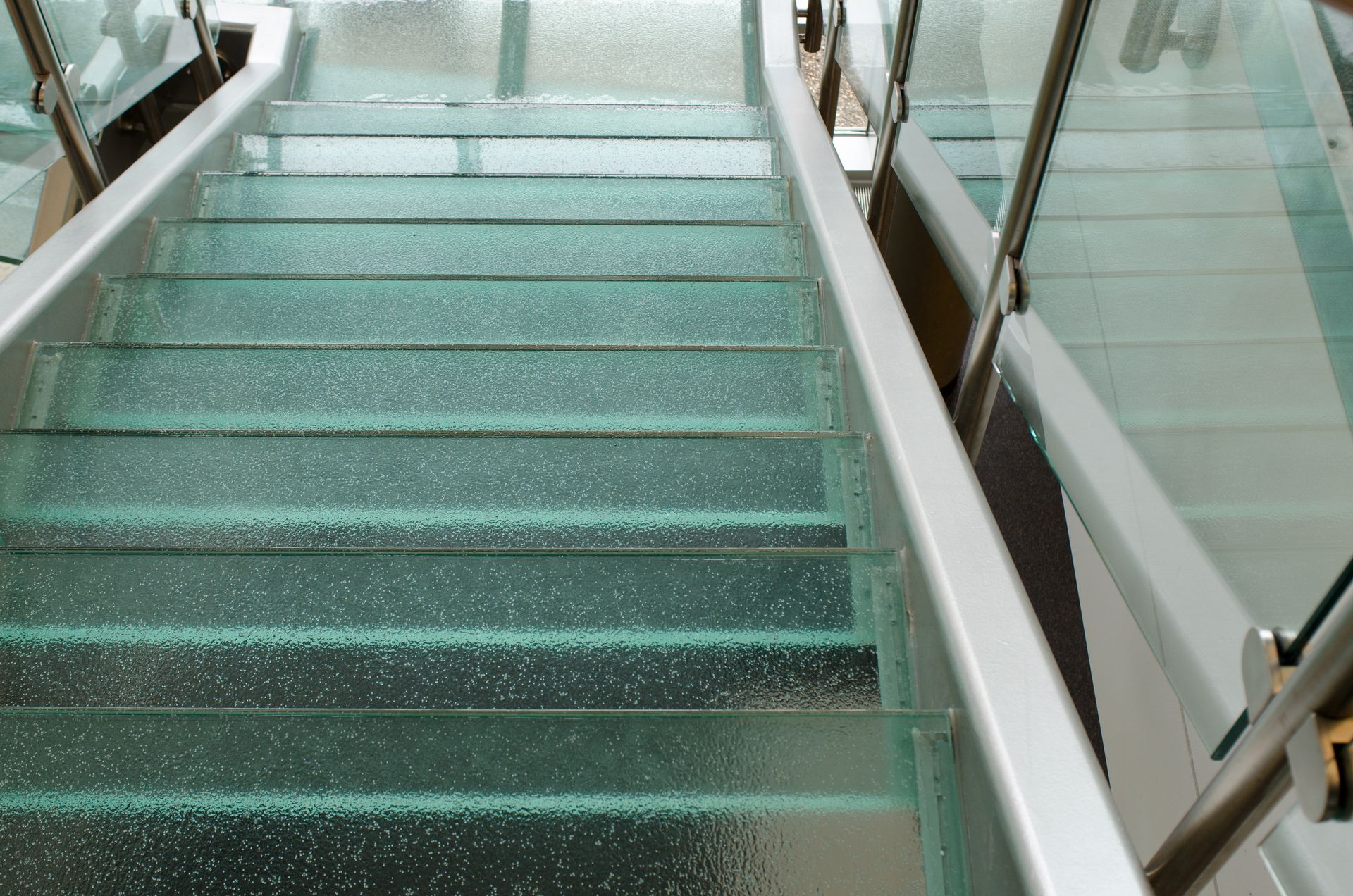 Glass stairway with turquoise steps and white railings in a modern interior