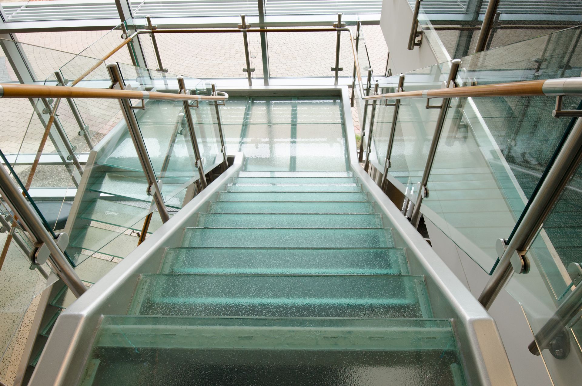 Glass staircase descending in a modern building with metal railings and frosted green steps