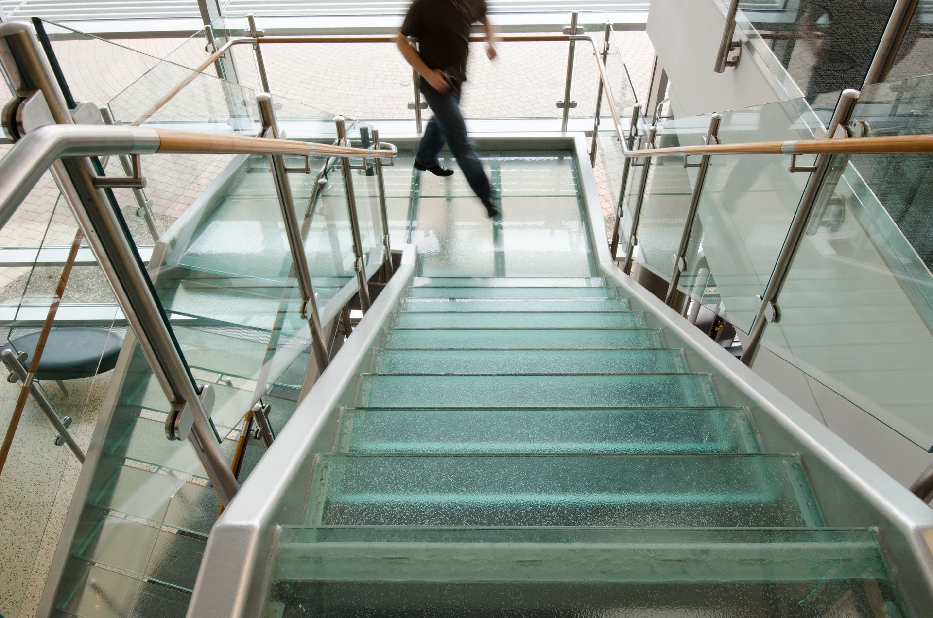 Glass staircase in a bright modern building, with a person walking down the stairs.