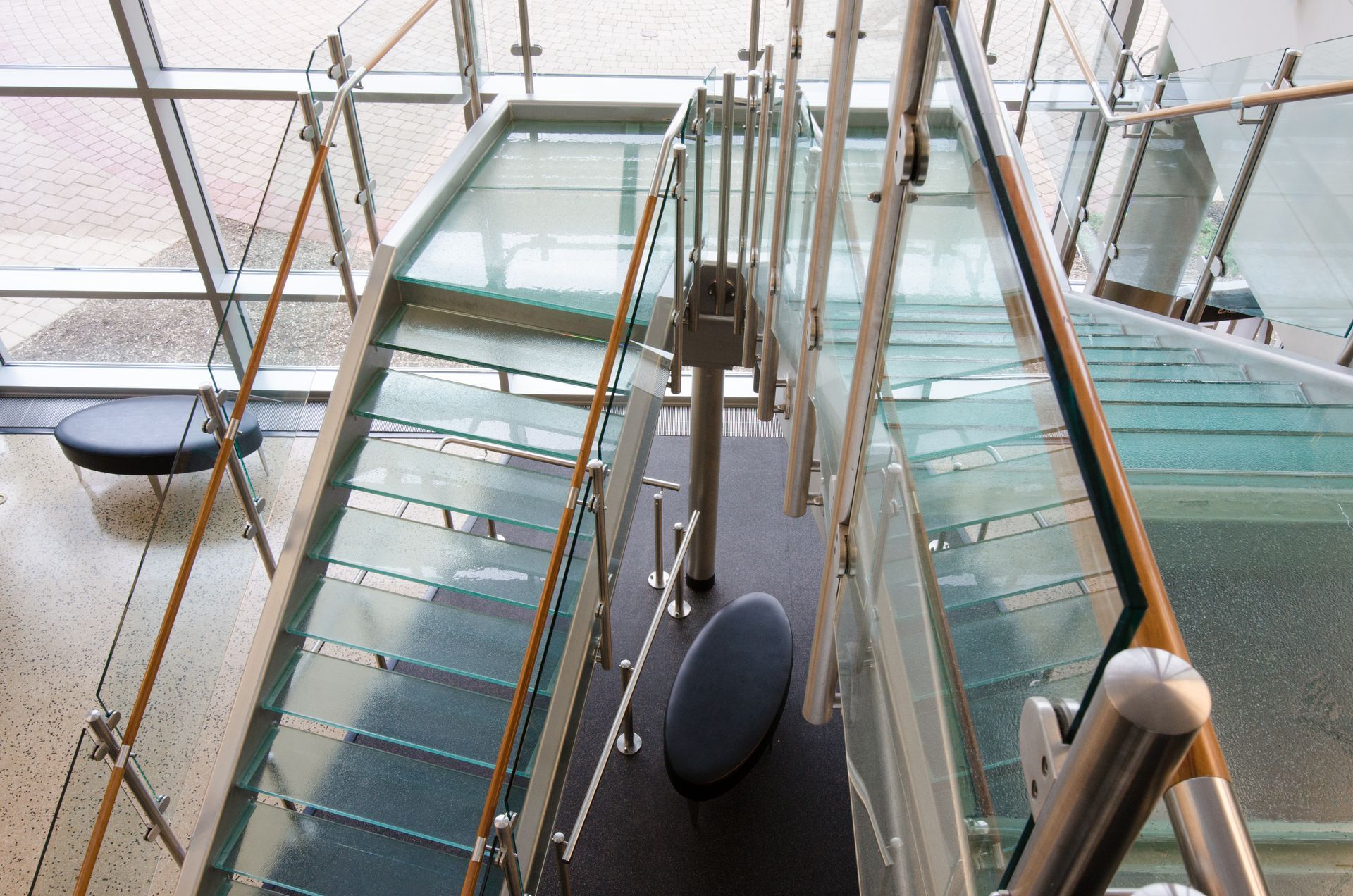 Modern glass-and-metal staircase with blue seats in a bright interior atrium