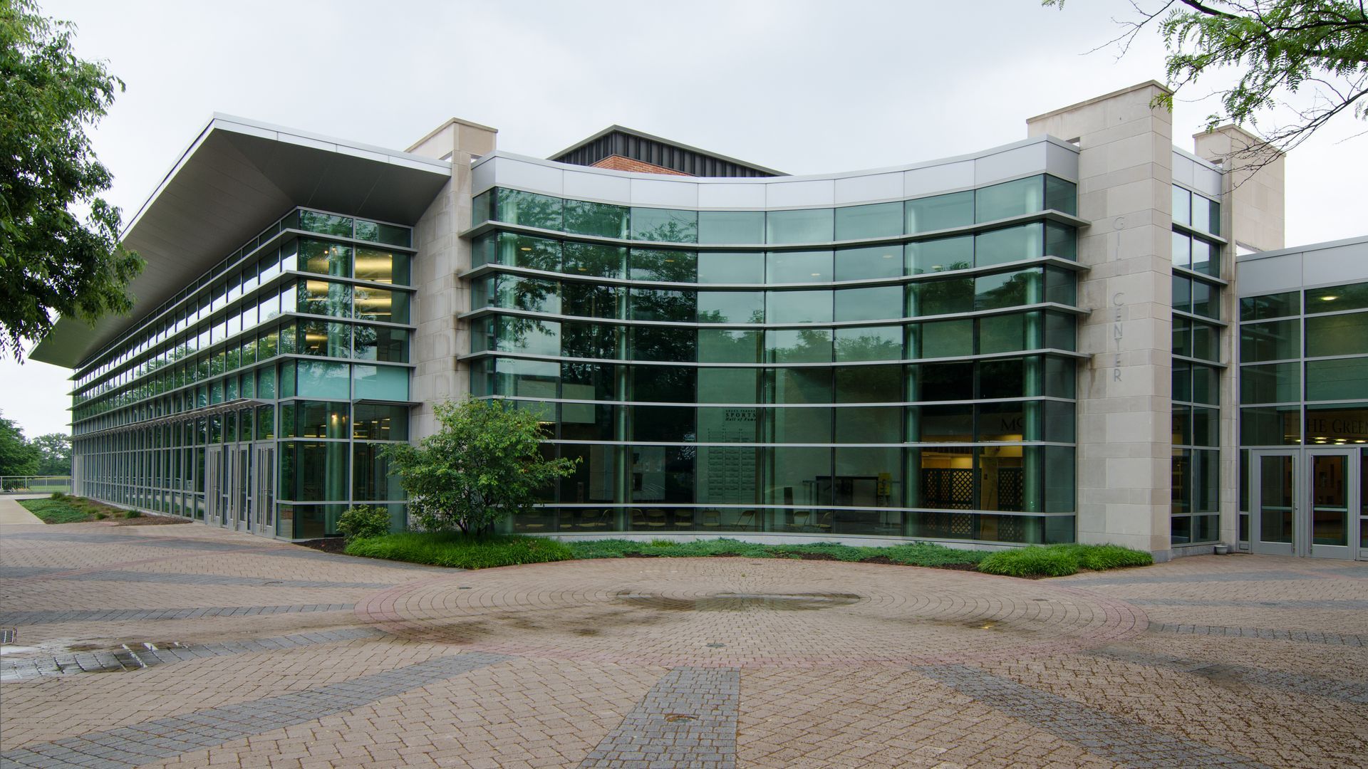 Modern glass-fronted office building with a curved facade and cobblestone plaza