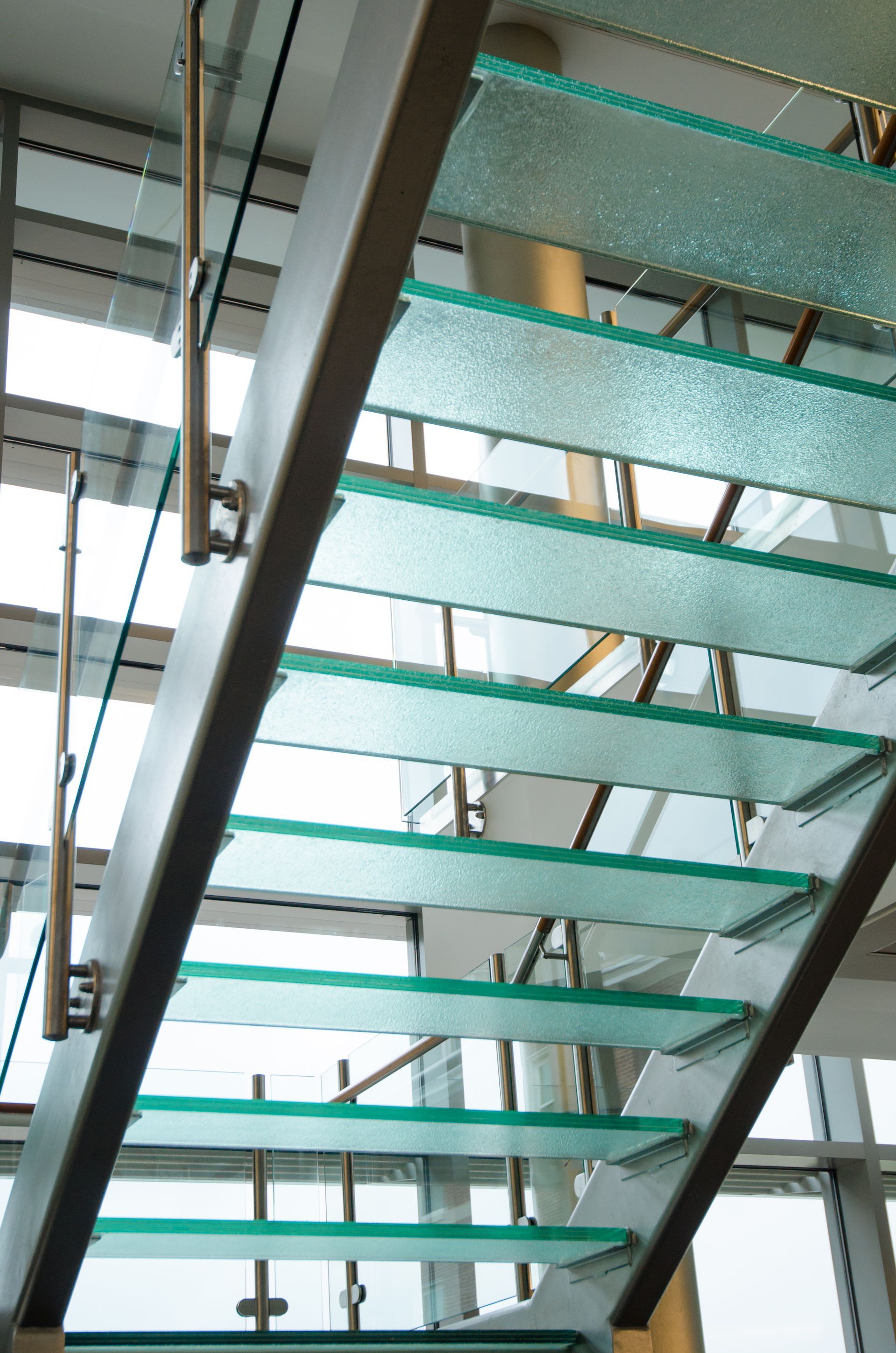 Glass staircase with turquoise steps and black railings viewed from below
