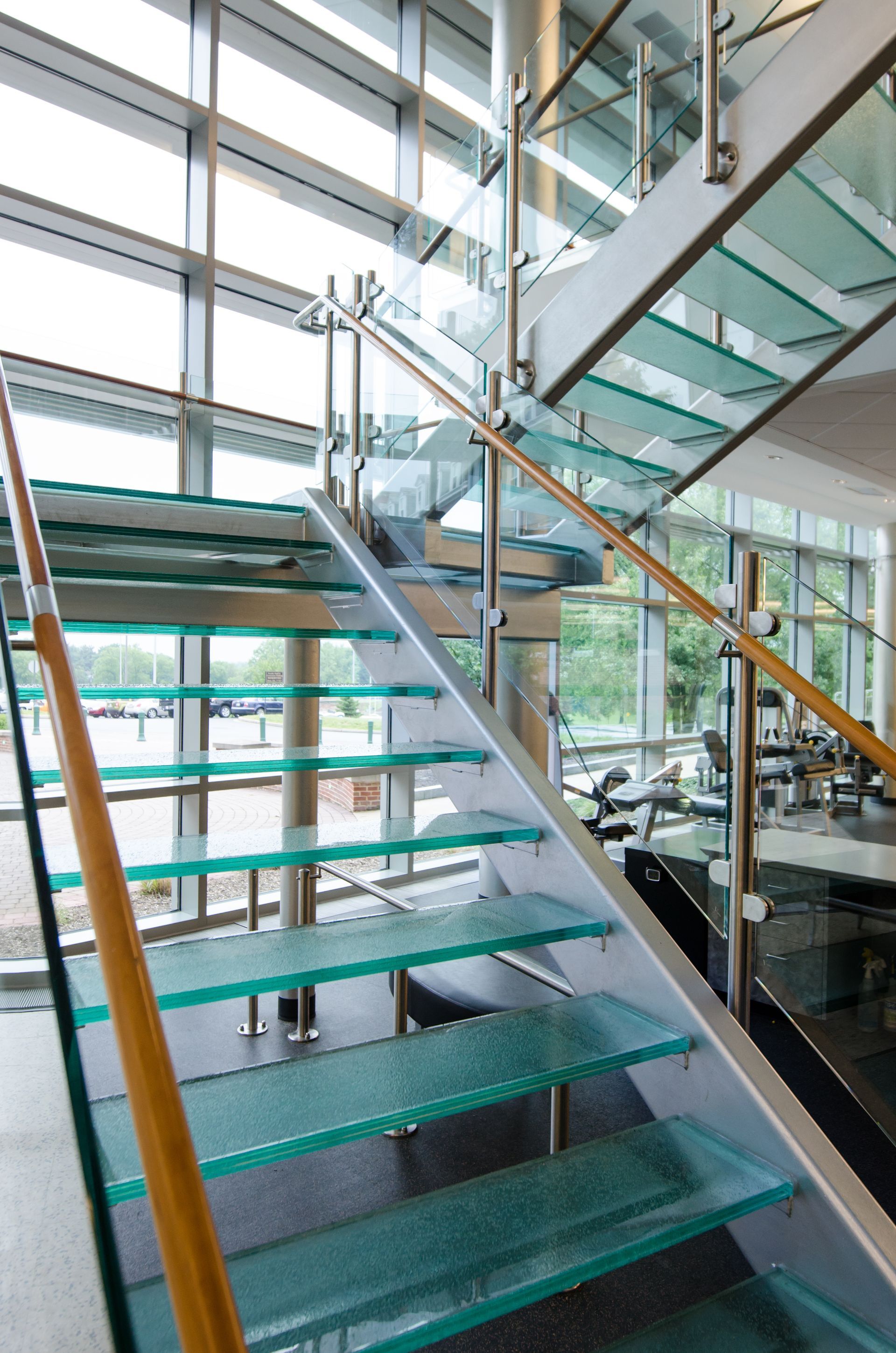 Modern glass staircase with turquoise steps and wooden handrails in a bright office lobby