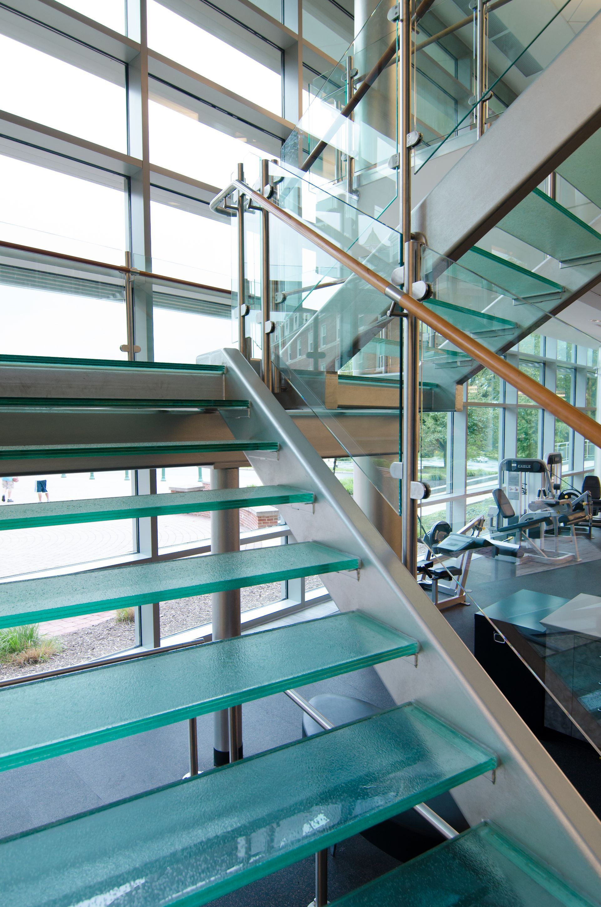Modern office stairway with glass railings and green-tinted steps beside a bright interior workspace