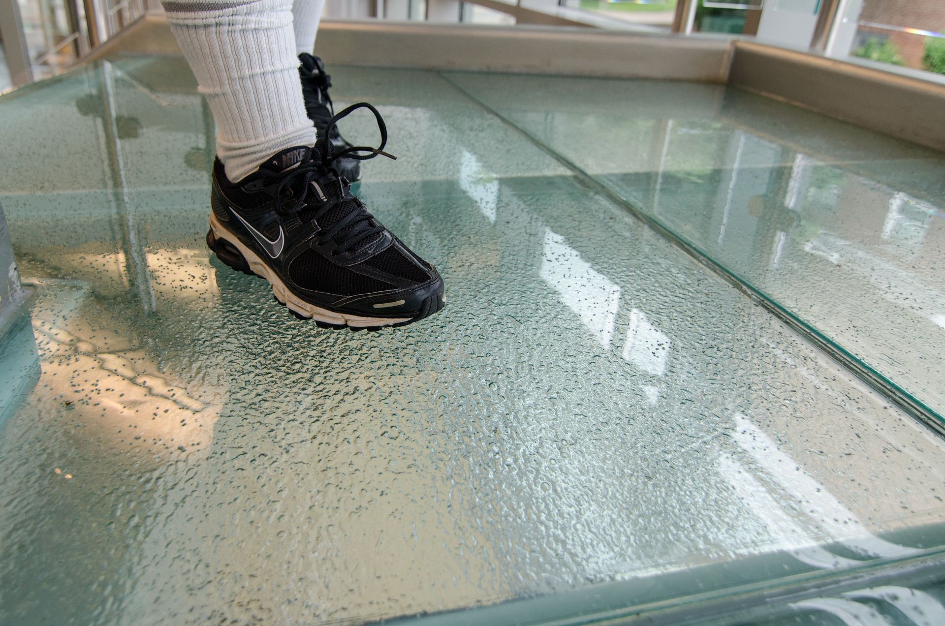 Person wearing black sneakers stands on a glass floor over water.