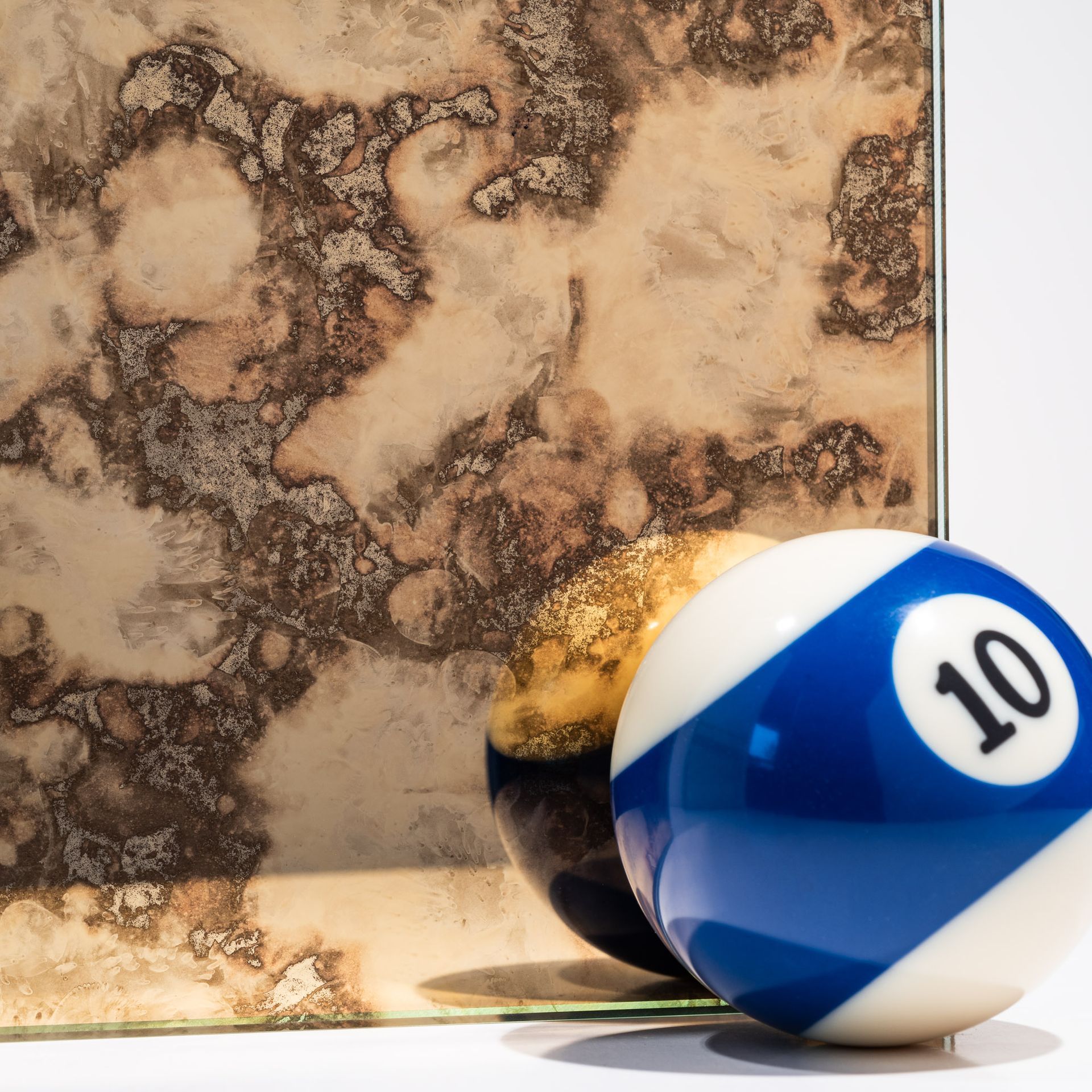 Blue-and-white billiard ball with 10 resting against a mottled tan background
