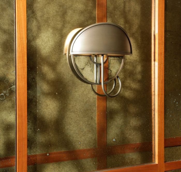 A metal outdoor wall lamp with a dome-shaped shade mounted on a custom antique mirror surface.